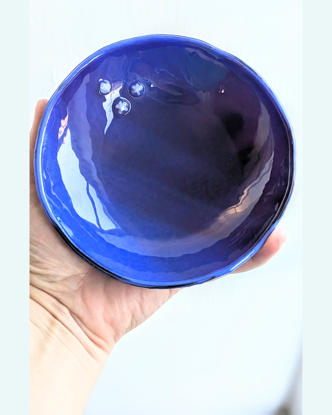 My hand holding a simple, cobalt blue glass bowl with three glass stars in on the top edge.