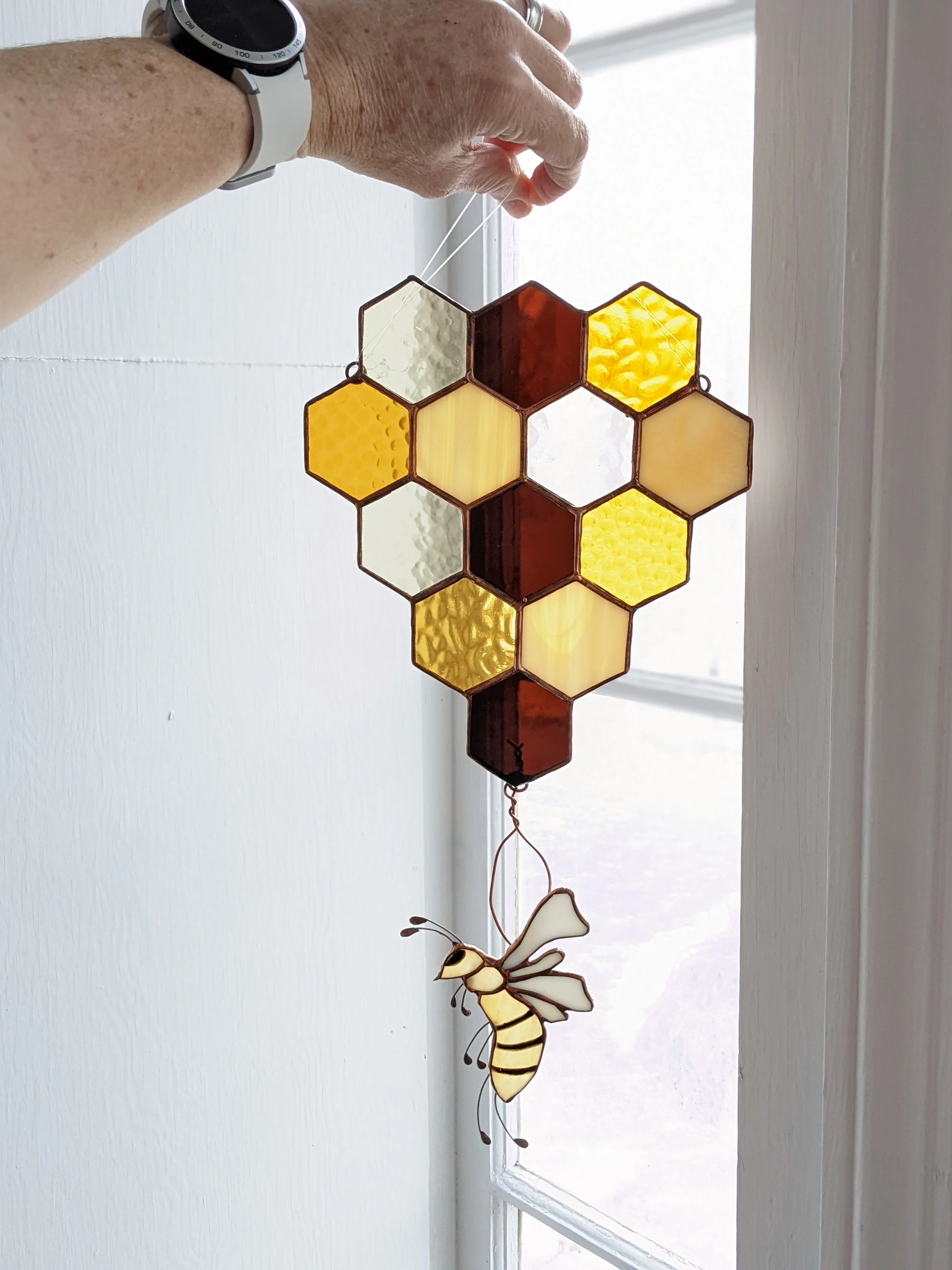 A free hanging honey comb of different amber and brown hues with a bee hanging at the end.