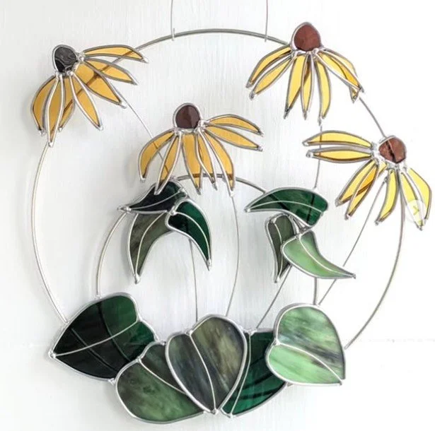 A lovely 3D stained glass piece of black eyed Susan flowers and leaves attached to two round metal rings.