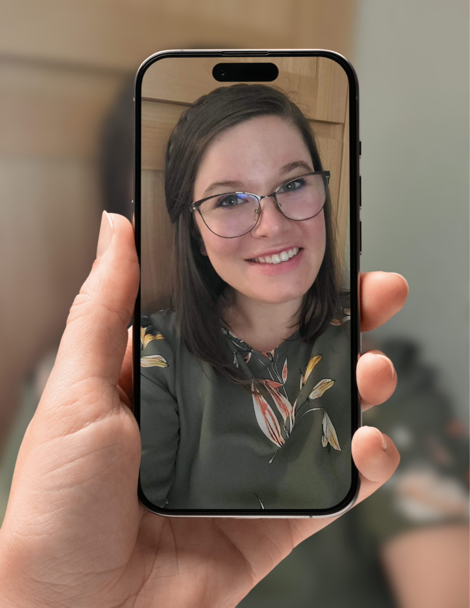 A person holding a smartphone displaying a selfie of a woman with brown hair and glasses, smiling at the camera.