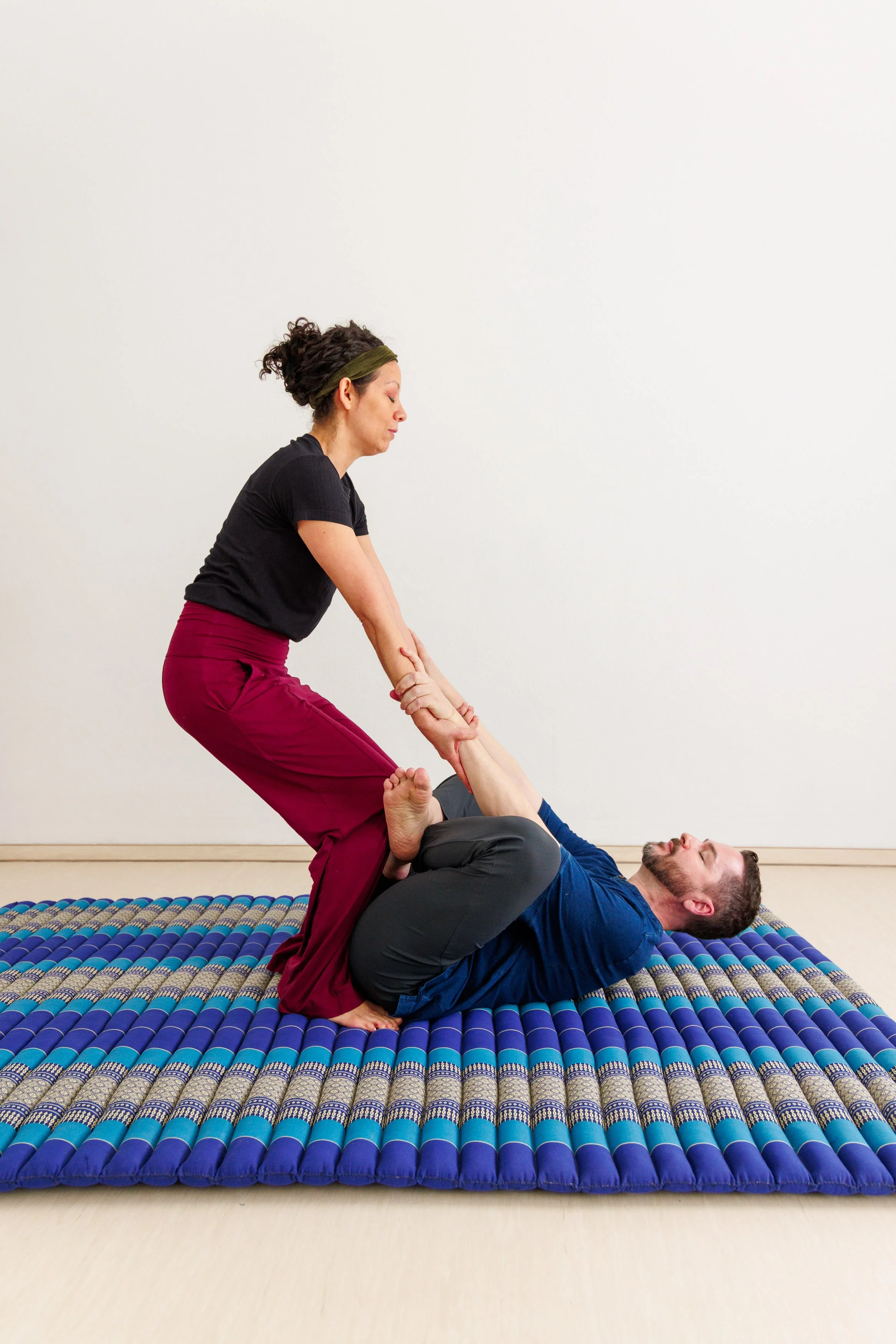 Eine Frau führt einen Partner-Yoga-Posenübung auf einer matten durch, während ein Mann auf dem Rücken liegt, beide halten sich an den Händen.