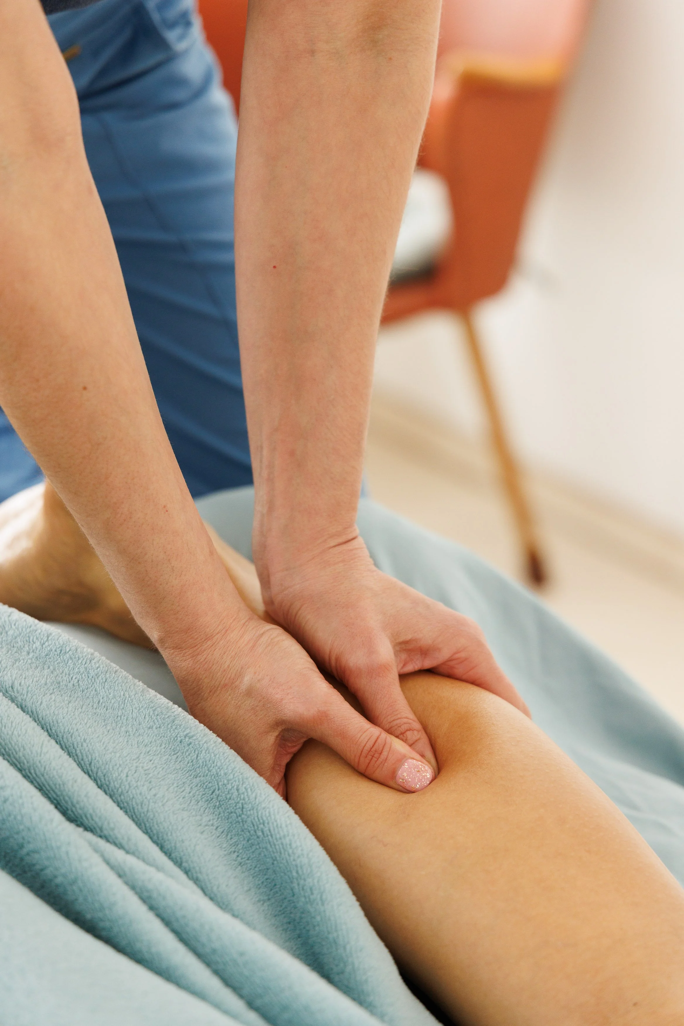 Eine Person erhält eine Beinmassage, die vom Fachmann durchgeführt wird, auf einem Behandlungsbett mit blauer Decke.