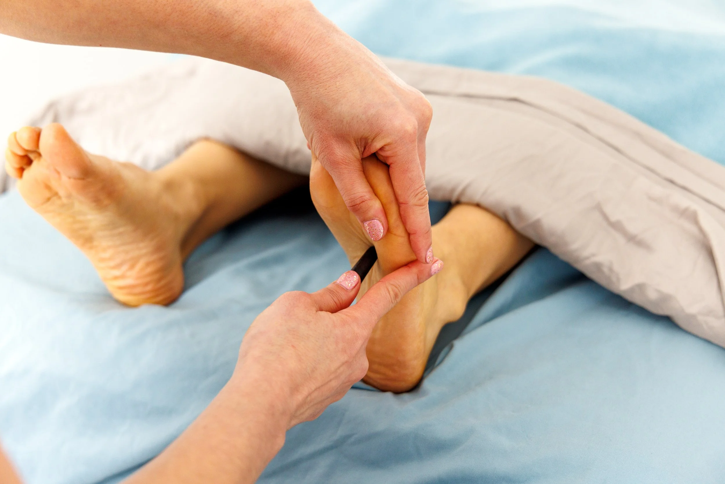 Fachkräftige Person führt eine Fußreflexzonenmassage am Fuß einer Patientin durch, die auf einer Behandlungsliege liegt.