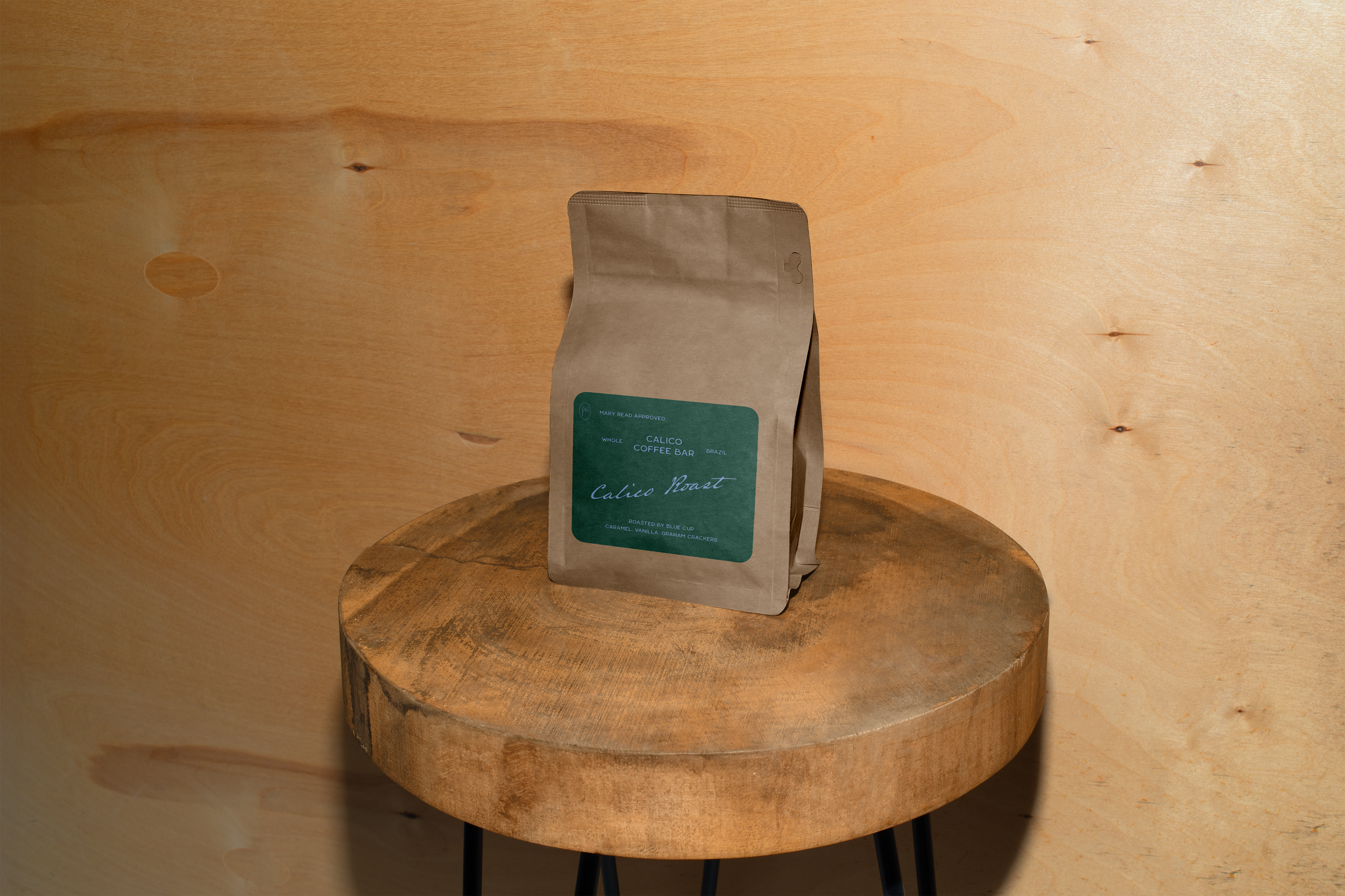 A bag of Calico Roast coffee by Blue Cup resting on a round wooden table against a wooden wall.