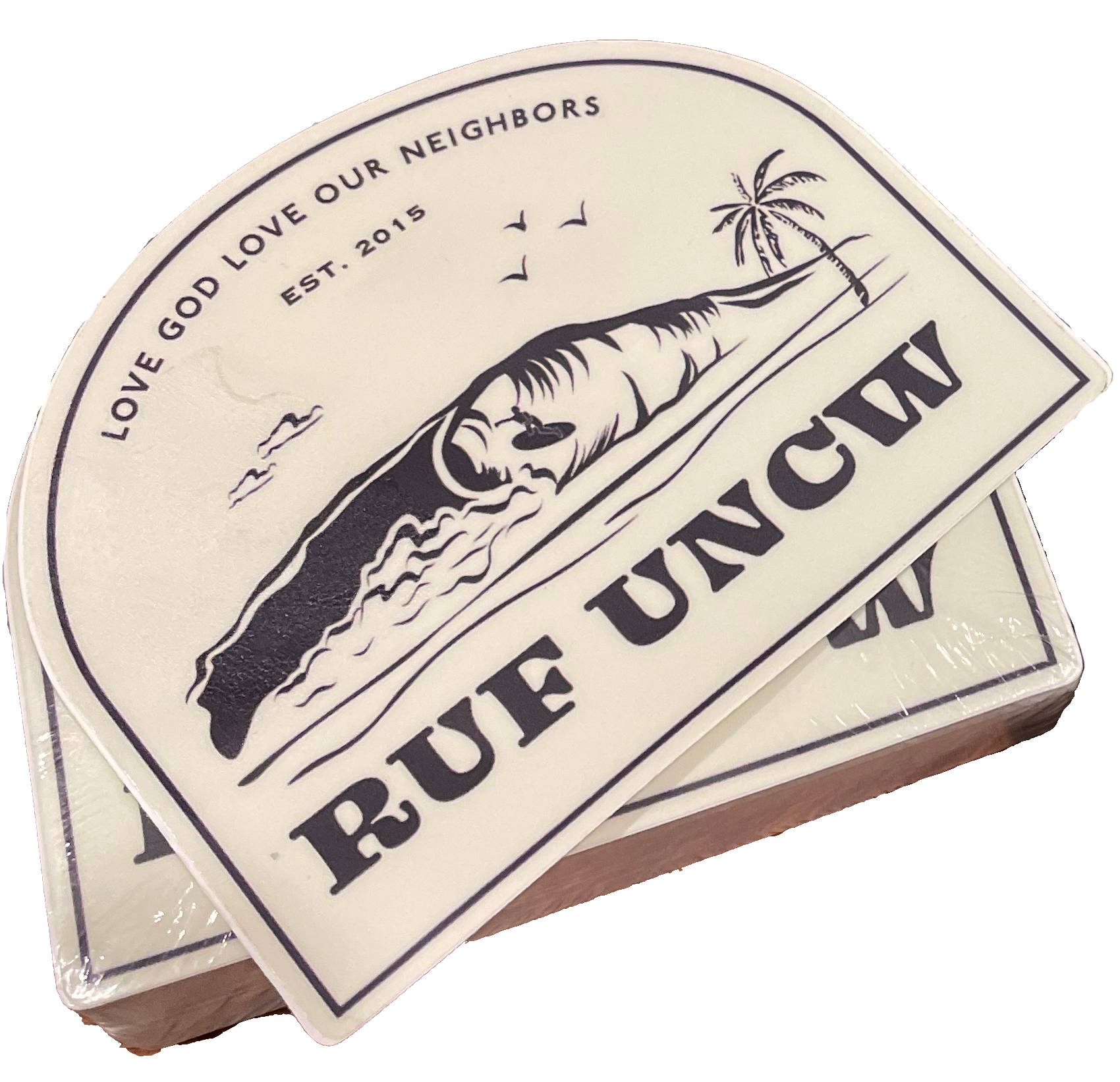 A stack of paper towels with a beach-themed logo featuring a wave, palm tree, and seagulls, and text reading 'Love God Love Our Neighbors, Est. 2015, RUE JUNCTION.'