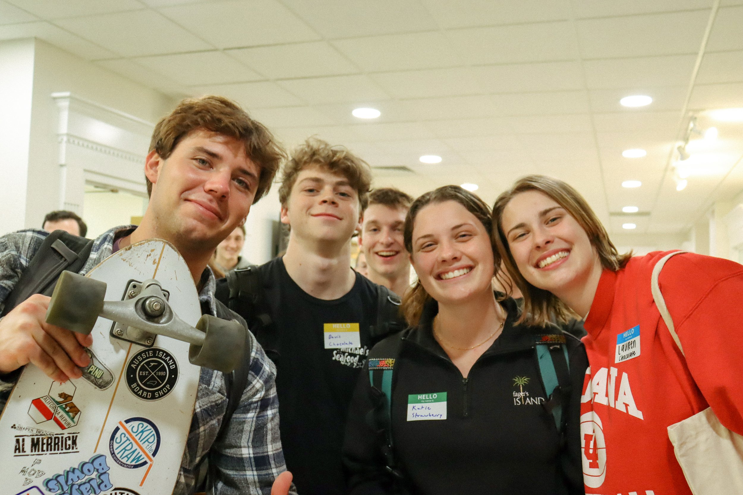 Group of young people smiling and taking a selfie at an indoor event, with some of them wearing name tags.