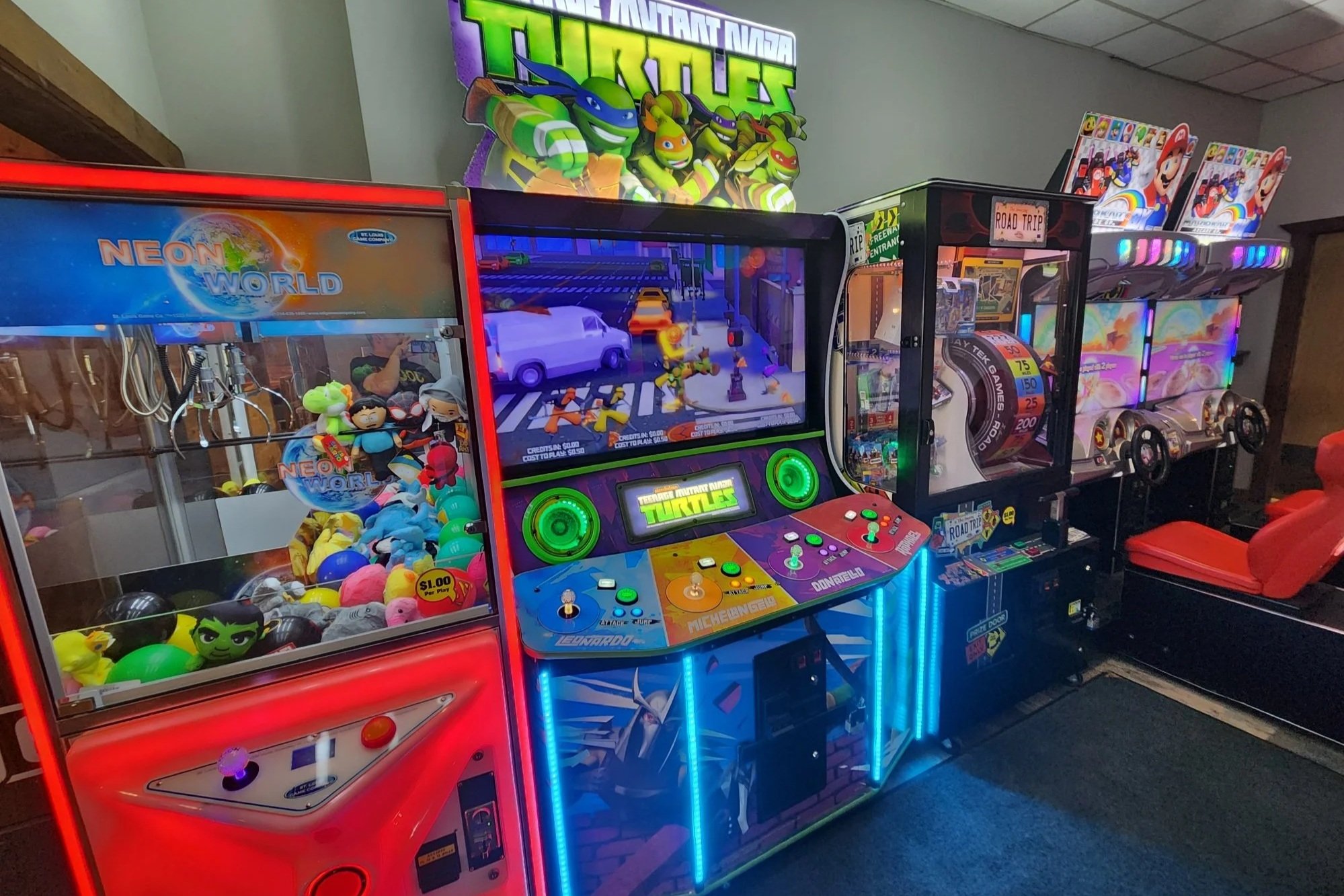 Arcade with various video games including a Teenage Mutant Ninja Turtles game, a claw machine filled with plush toys, and other arcade machines with colorful lights.