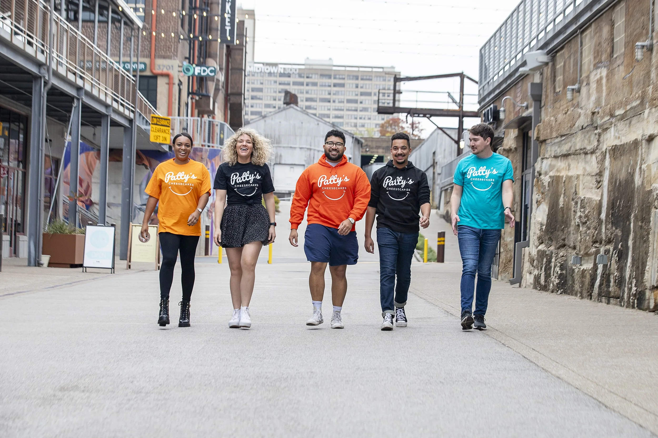 Five young adults walking together in an urban area, smiling and enjoying each other's company.