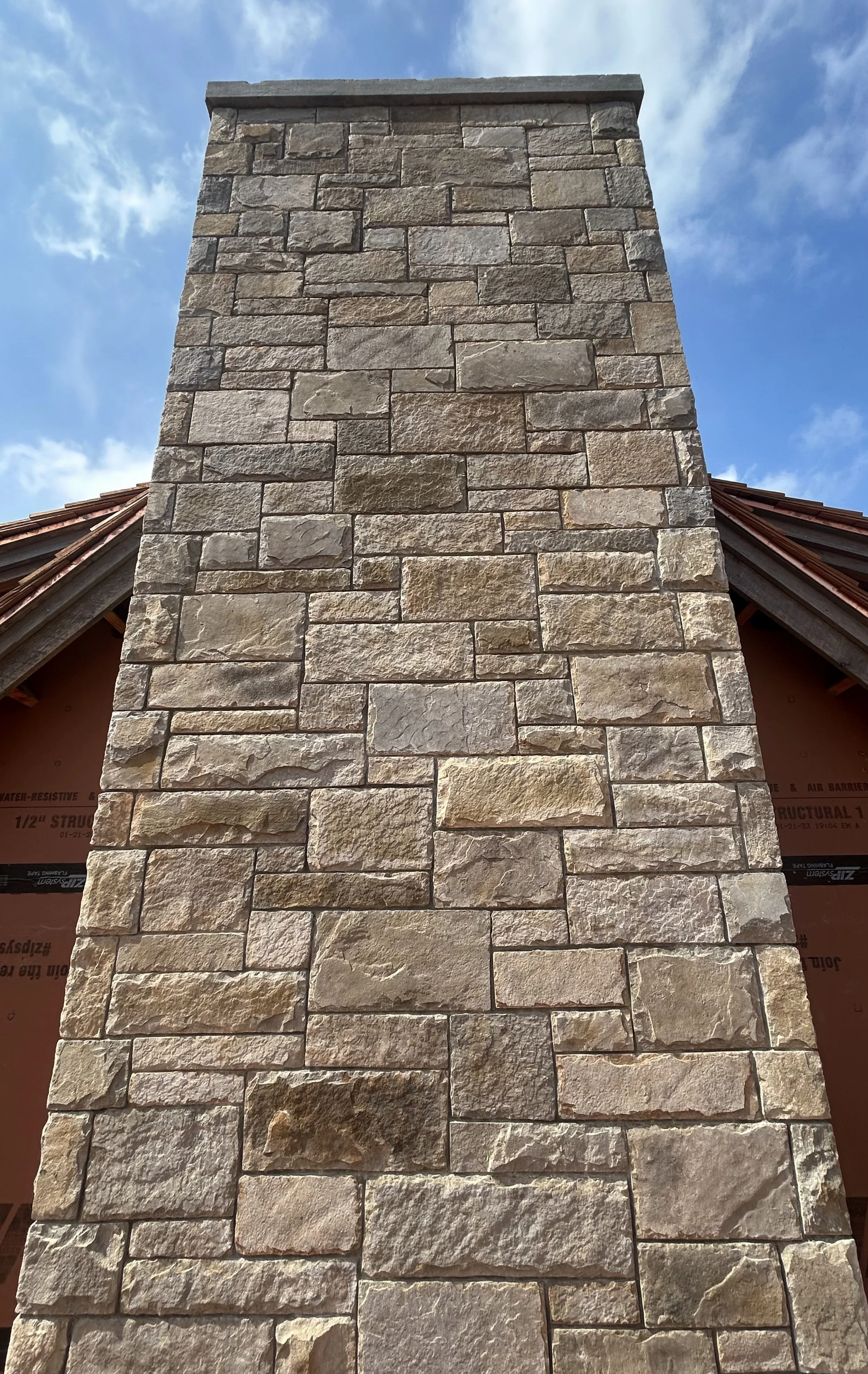 Close-up of a large stone chimney with a blue sky and clouds in the background.
