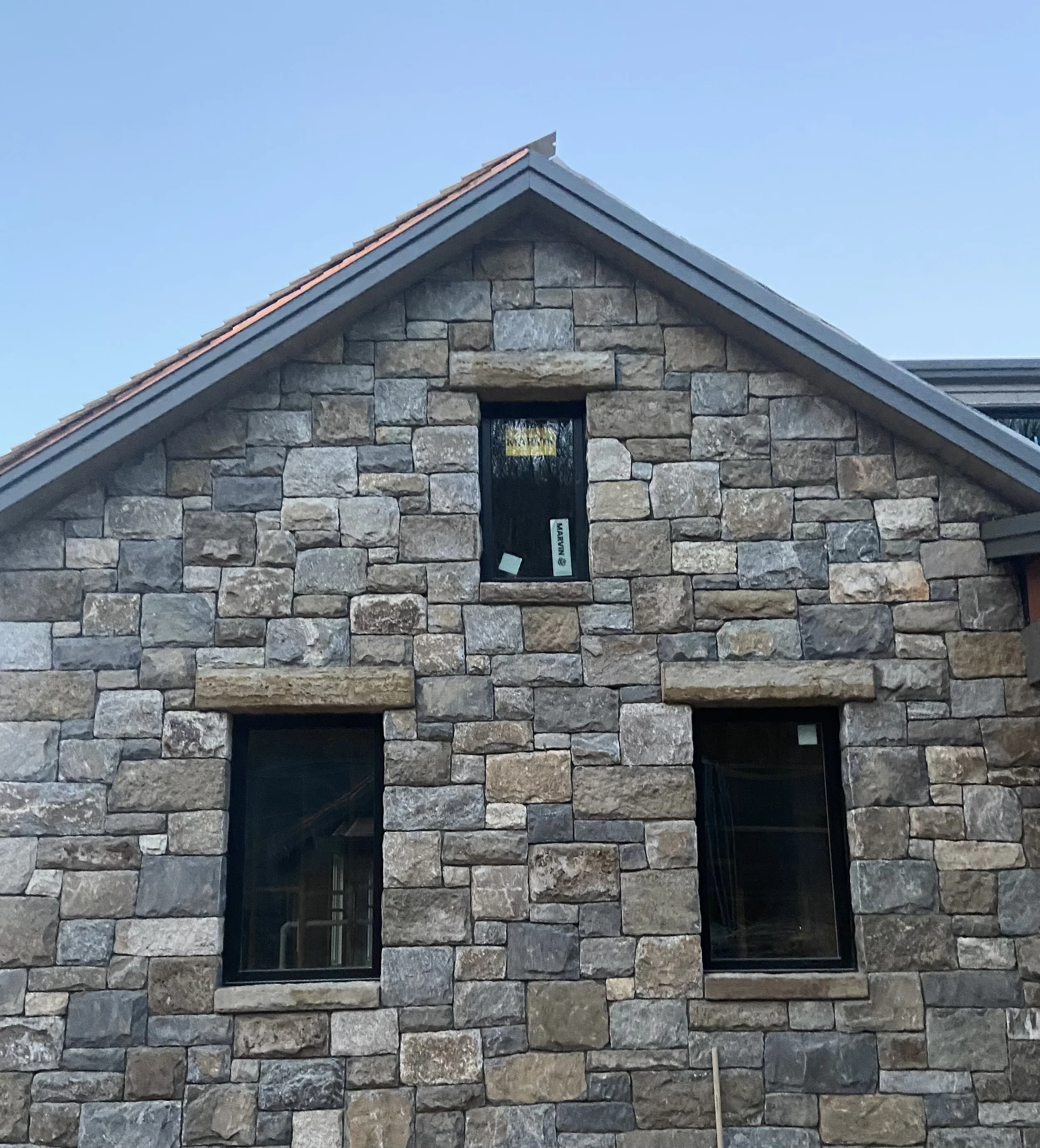 Close-up of a stone house wall with three black-framed windows and a gabled roof.