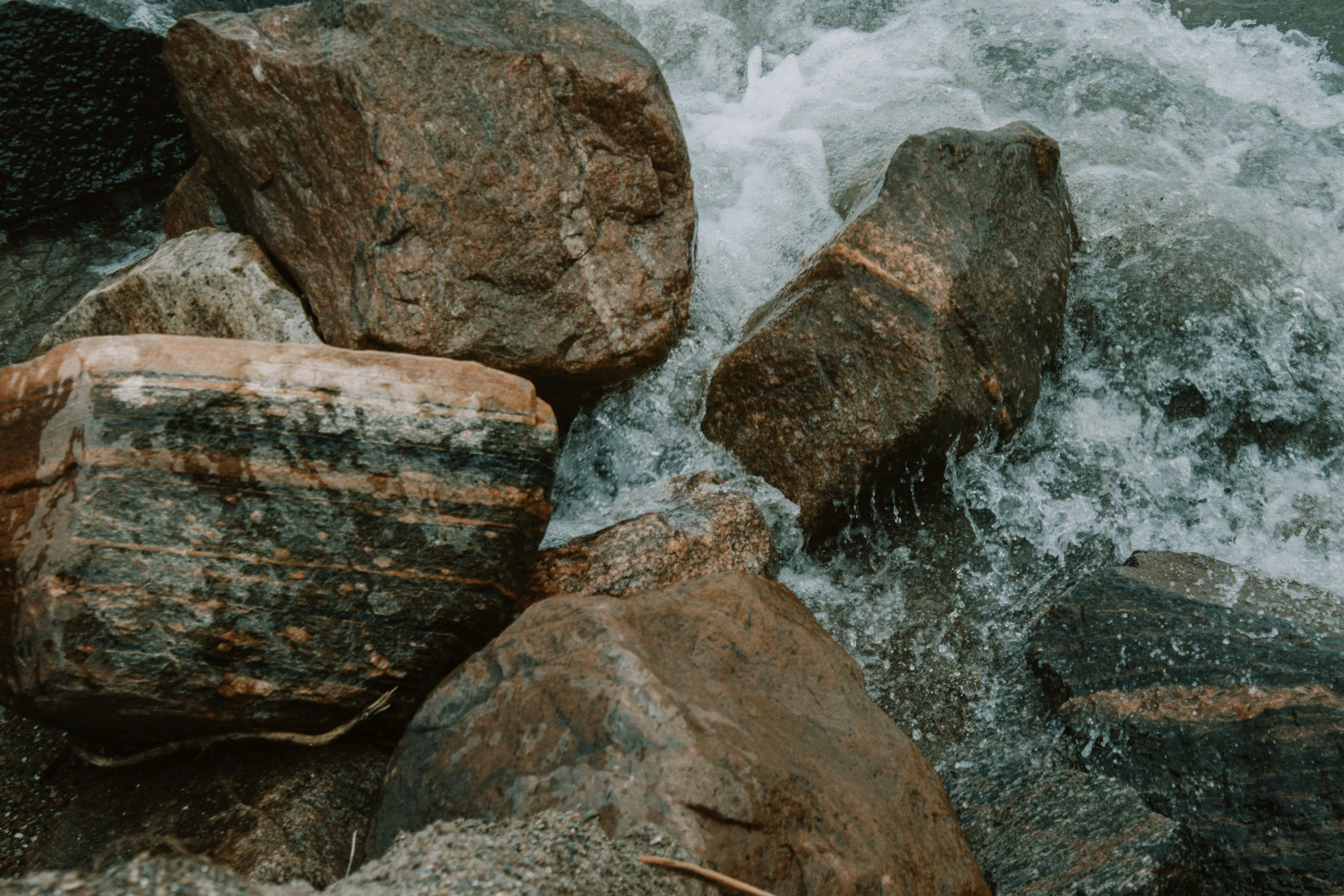 Close-up of rocks in a flowing river, with water splashing around them.