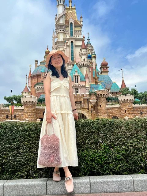 Woman in a white dress and wide-brimmed hat standing in front of a Disney castle at Disneyland.