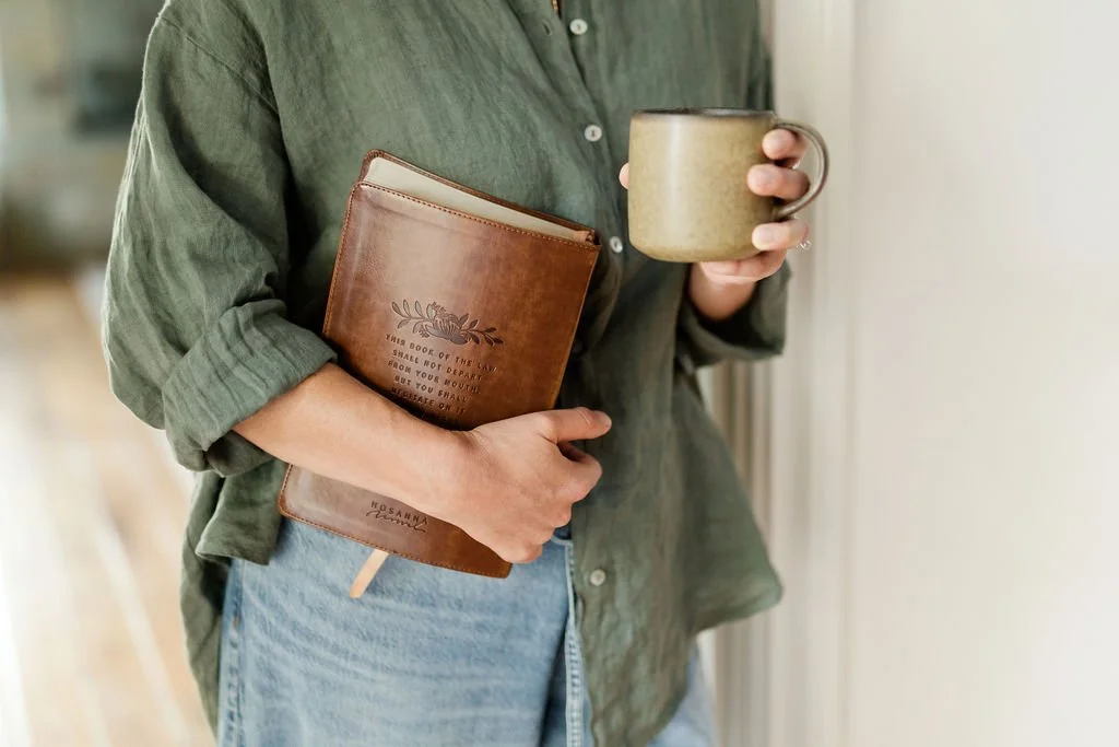 Person in green shirt holding a coffee mug and a brown leather journal.