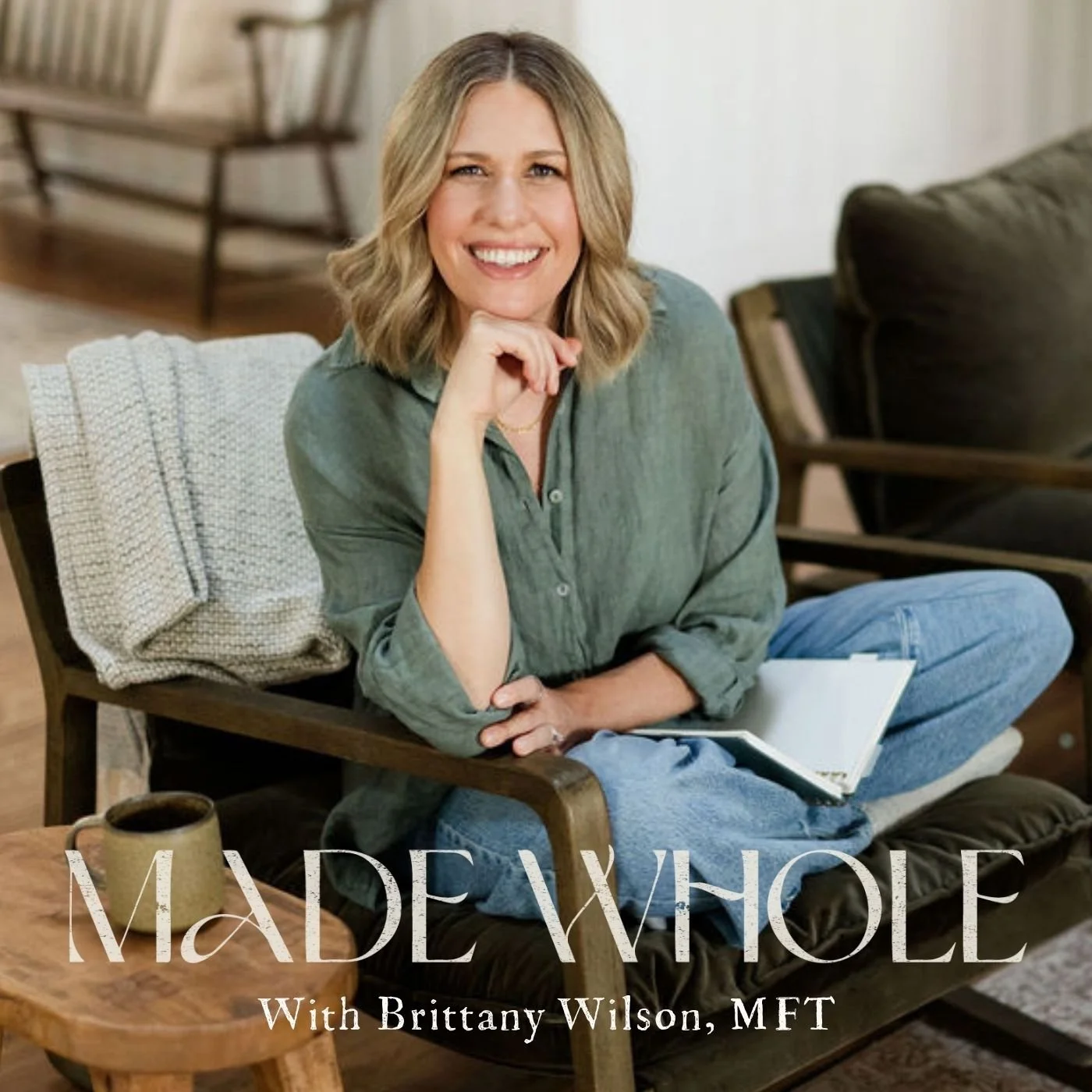 A woman with blonde hair smiling sitting in a cozy living room, holding an open notebook, with a mug on a wooden table nearby. Text on the image reads 'MADE WHOLE with Brittany Wilson, MFT.'