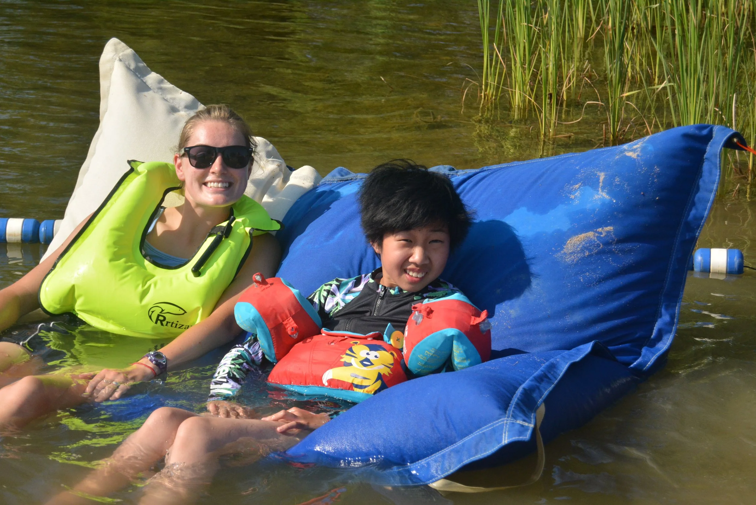 Child and adult enjoying lake with floatation devices.