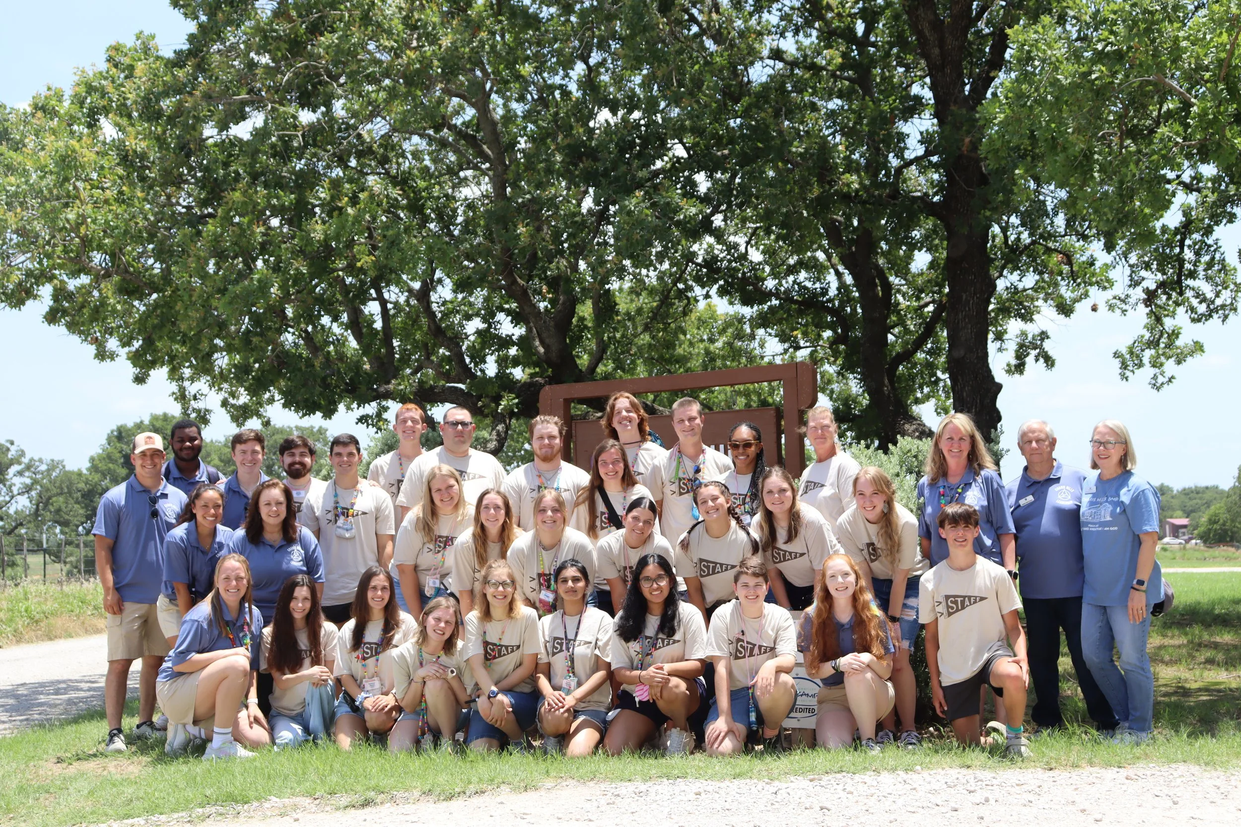 A large group of students and leaders smiling and posing outdoors under trees, indicative of a successful Campus Ministry retreat.