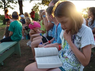 Young girl reading the bible at outdoor summer camp