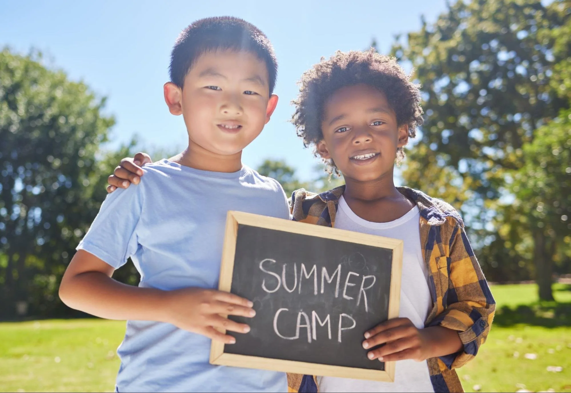 Two boys pose for a photograph, holding a board that reads "Summer Camp."