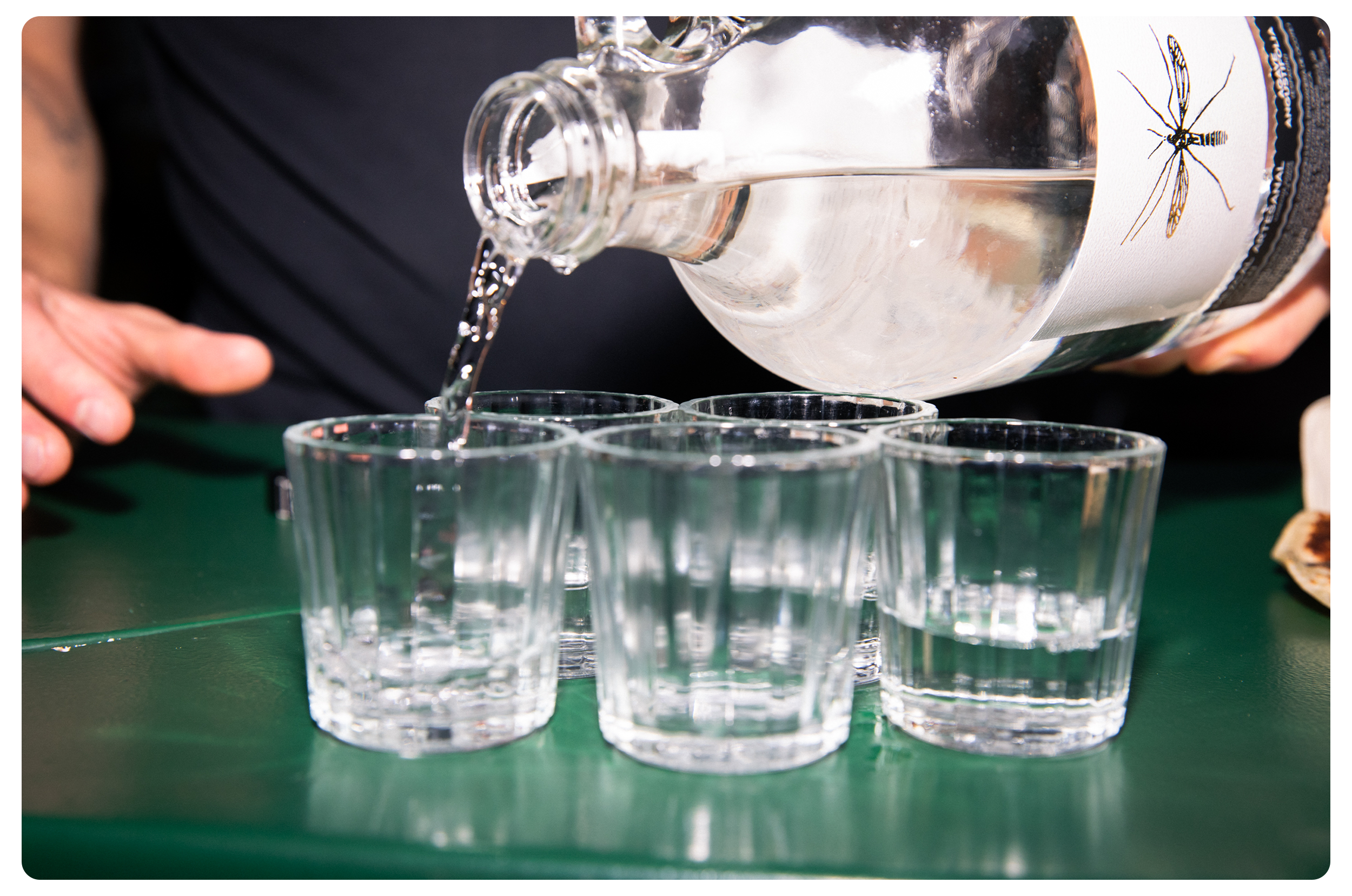 Person pouring water from a bottle into one of three glasses on a green surface.