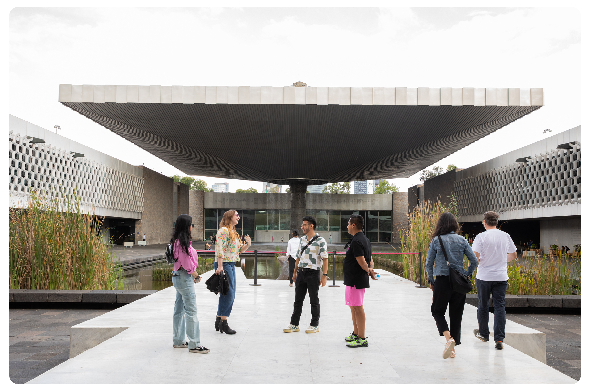 Group of seven people standing and chatting outdoors near a modern architectural building with water features and greenery.