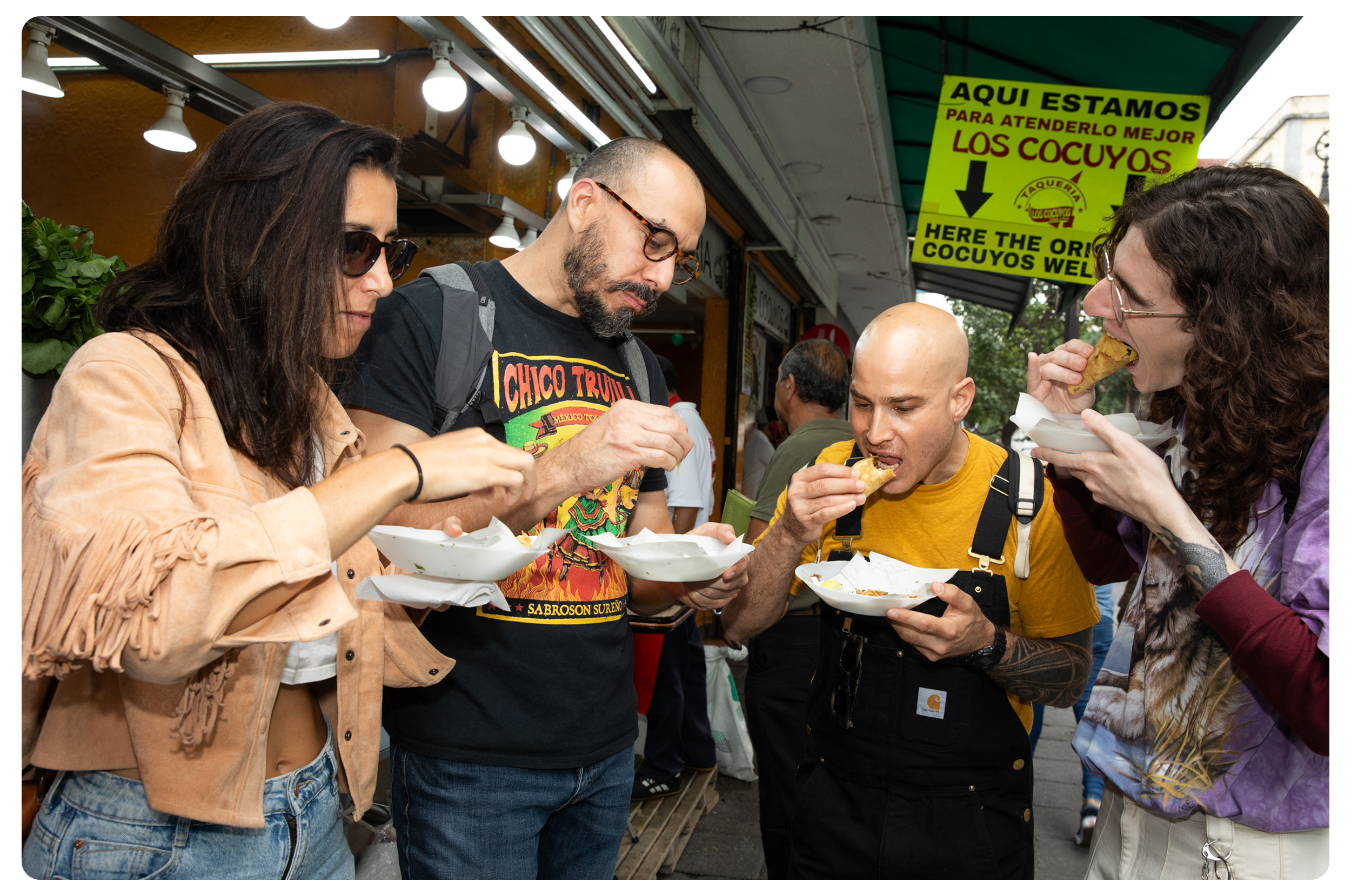 Four people eating tacos at a food stand on a busy street.