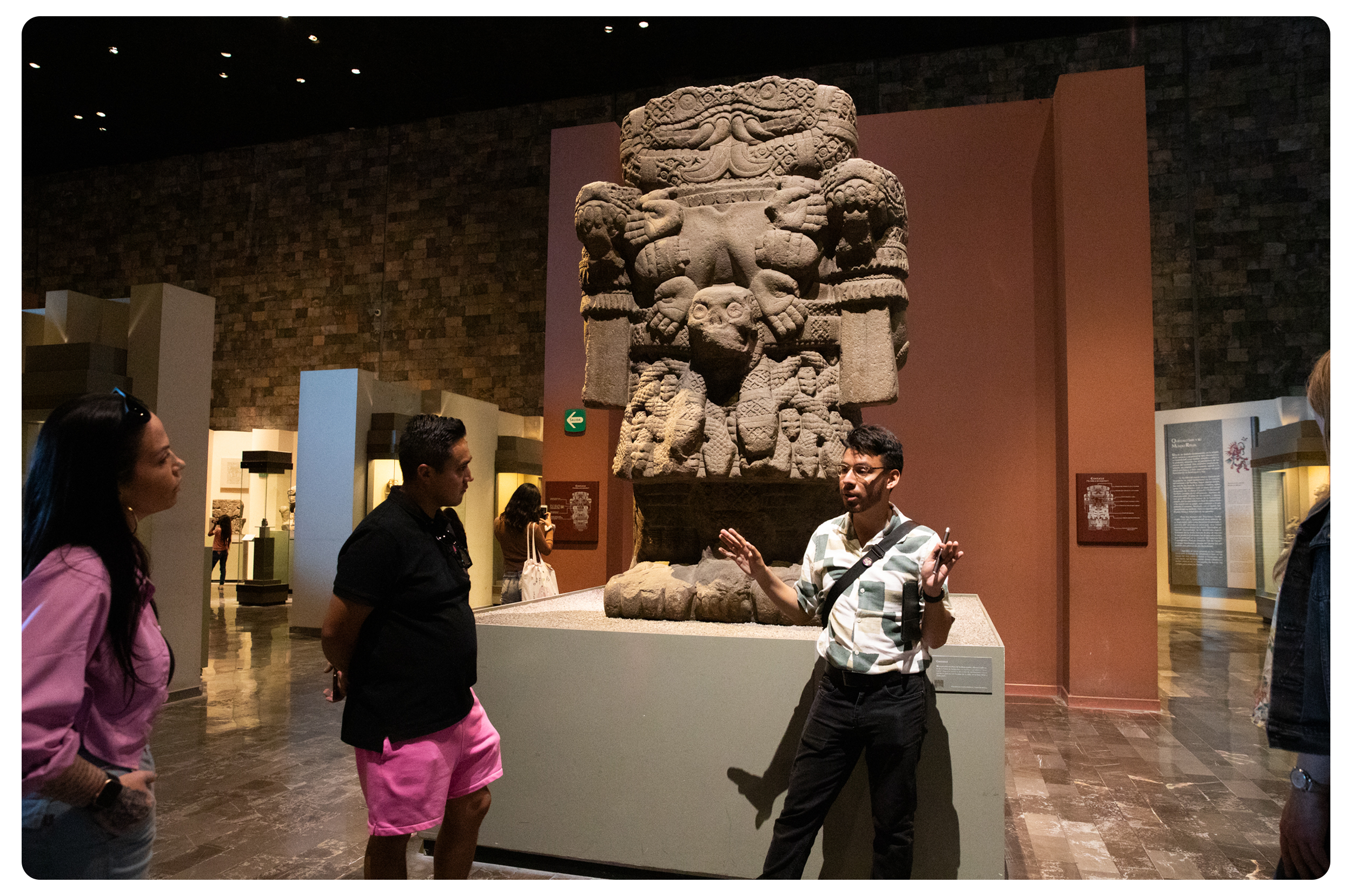 A museum visitor explains ancient stone sculpture carvings to visitors in a museum exhibit.