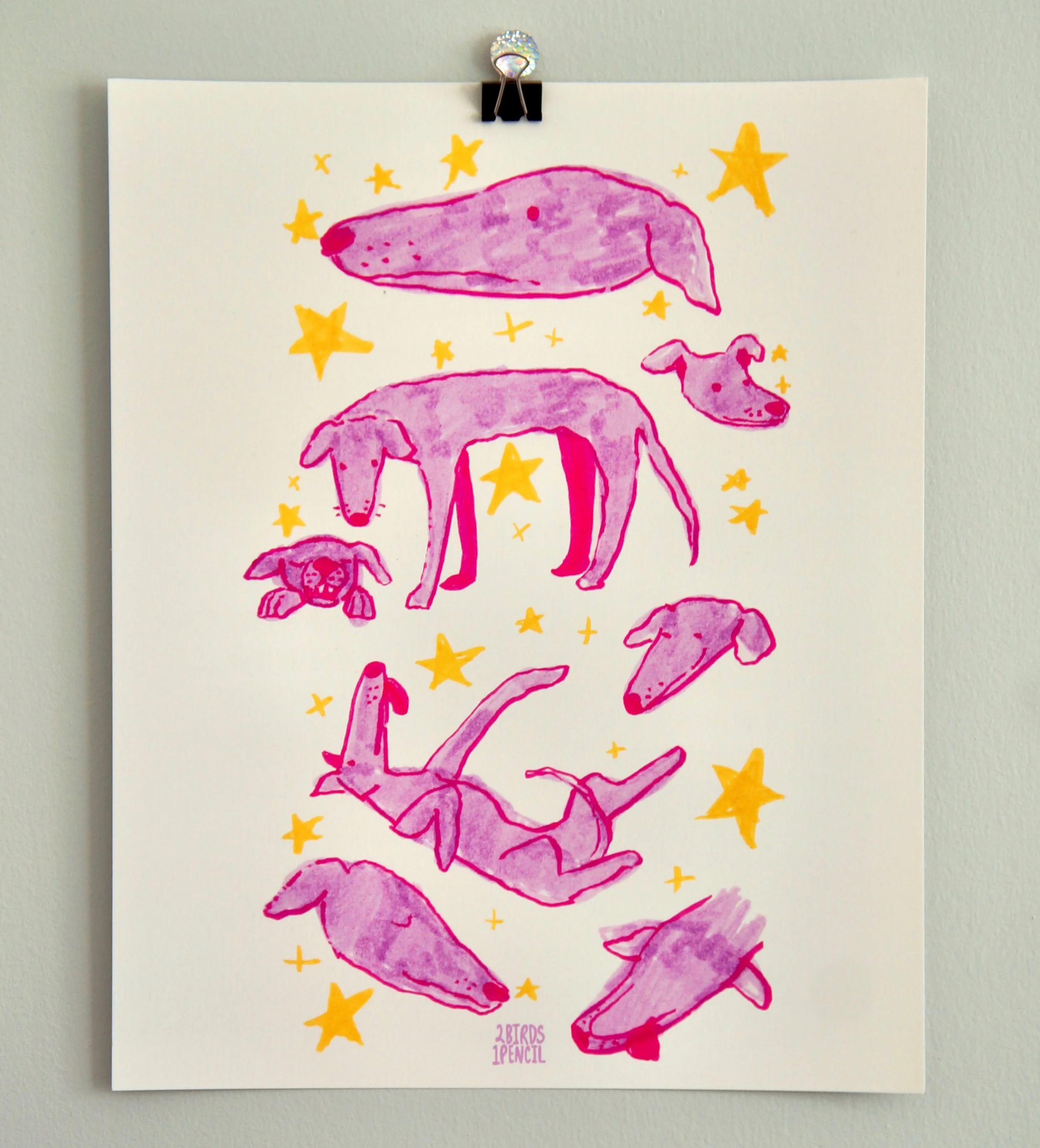 An art print hanging on a wall. The design is a sketchbook page of silly greyhound doodles drawn in pink and purple marker, surrounded by yellow stars.