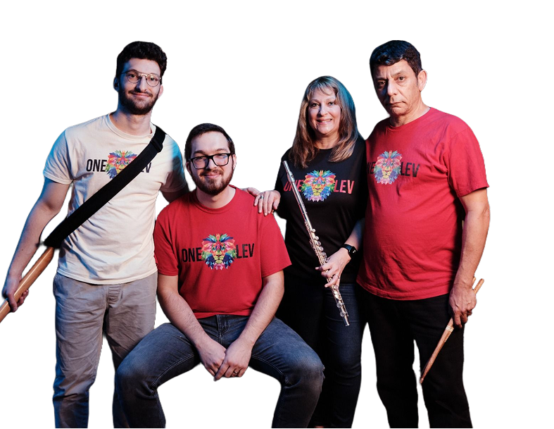 Four people, two men and two women, posing together against a black background. They are wearing casual clothing, and some are holding musical instruments, including a flute and drumsticks. Three of them are wearing matching t-shirts with a colorful heart and the words 'ONE LOVE' on them.