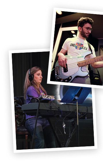 A woman with long hair wearing headphones and a purple shirt playing a keyboard, and a man with glasses and a beard playing a bass guitar, in a music studio or rehearsal space.