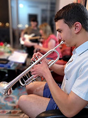 Young man playing trumpet in a group setting with others in the background.