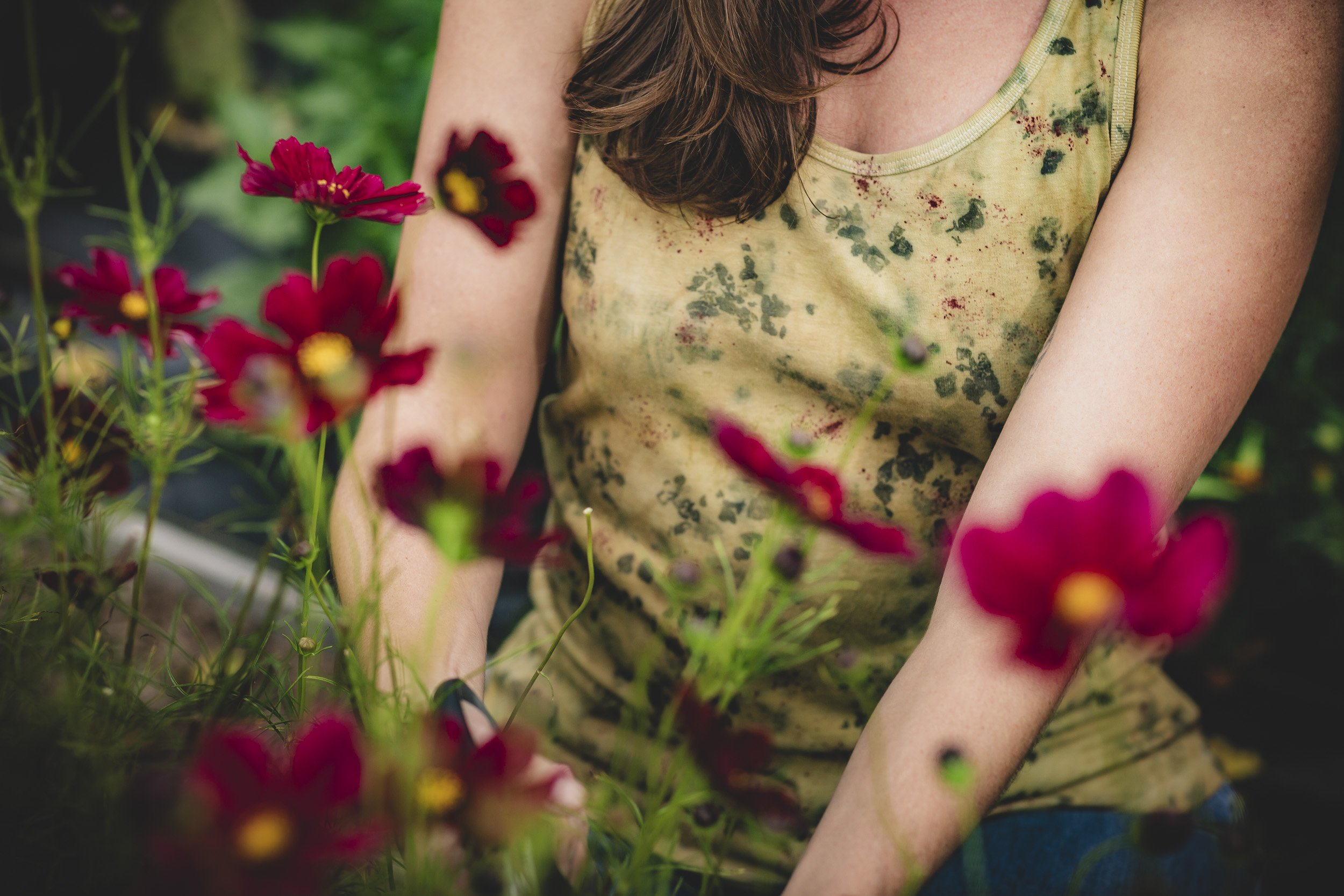 A woman with brown hair wearing a yellow sleeveless top with a splatter pattern, surrounded by red flowers.