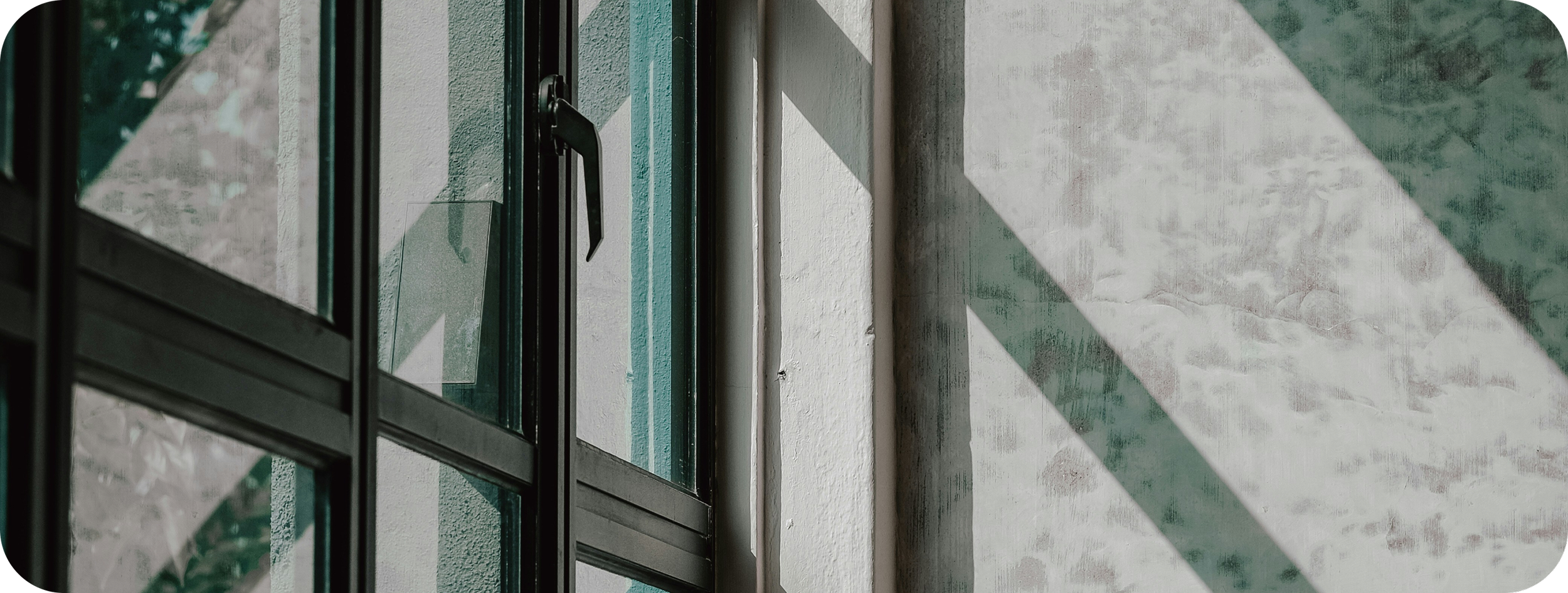 Close-up of a glass door with a black handle, casting diagonal shadows on a textured white wall.