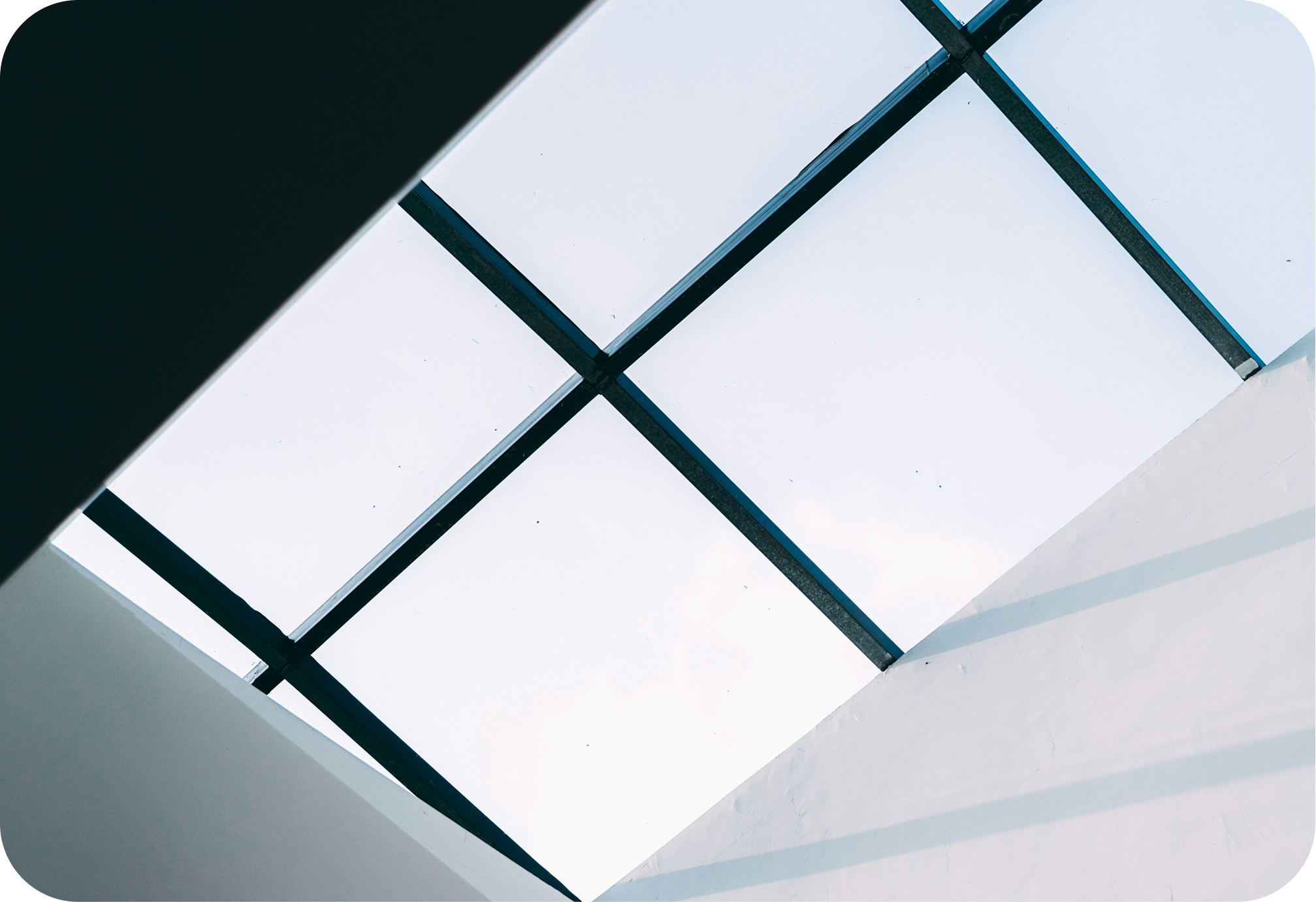 View of a glass ceiling or skylight with black framing, with a bright sky visible through the glass panels.