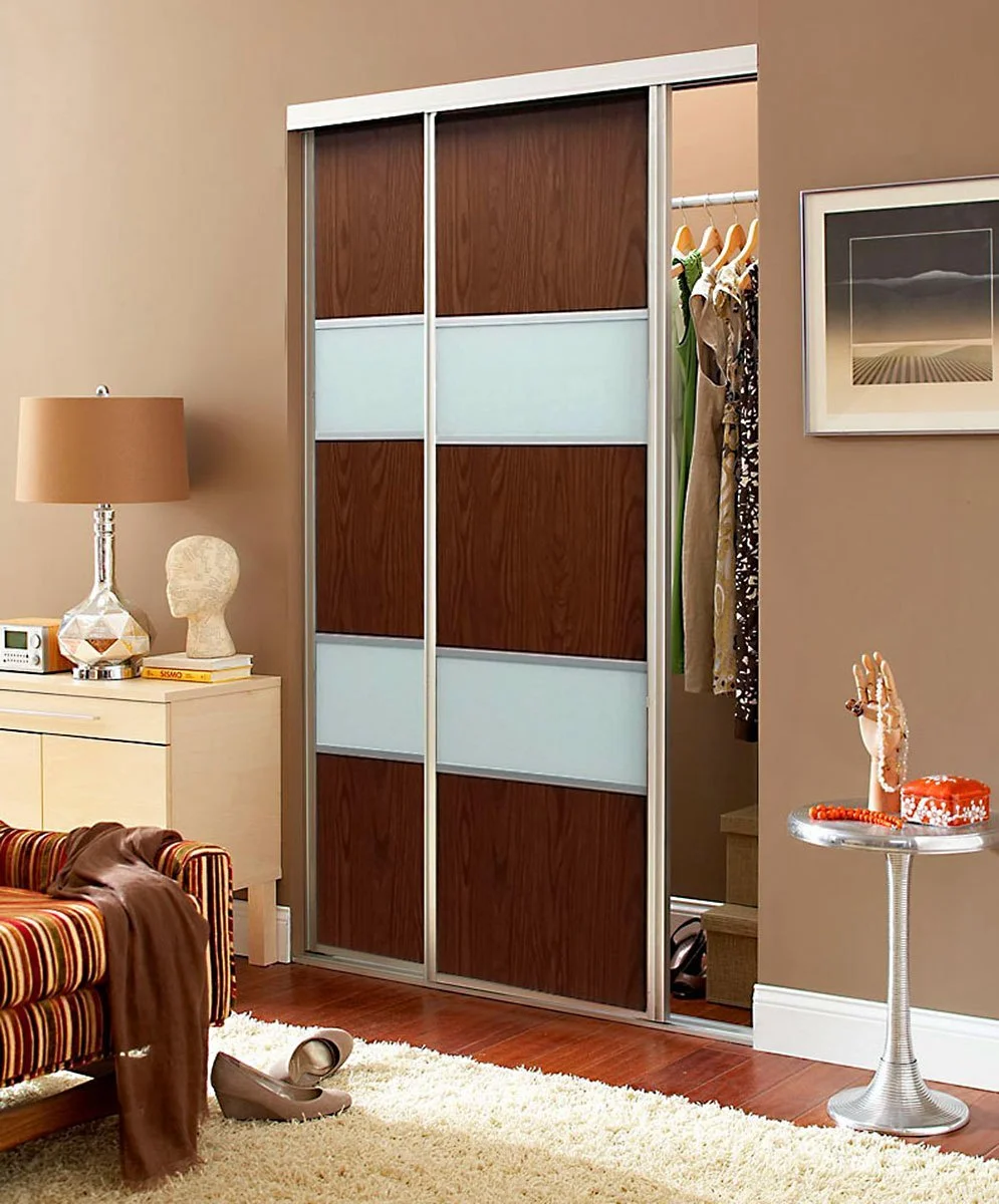 A sliding closet door with wood and frosted glass panels in a bedroom with beige walls and hardwood floors.