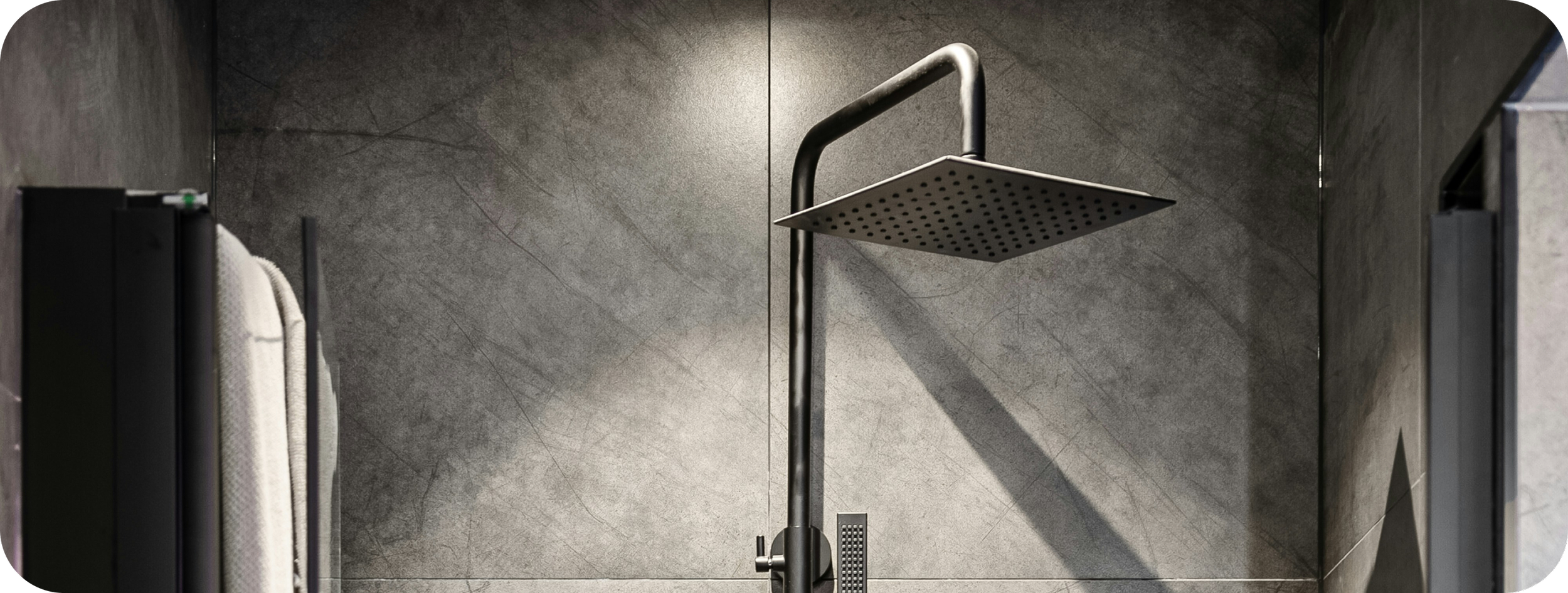 A modern shower with a large square rain showerhead mounted on a metallic pipe against a gray tiled wall.
