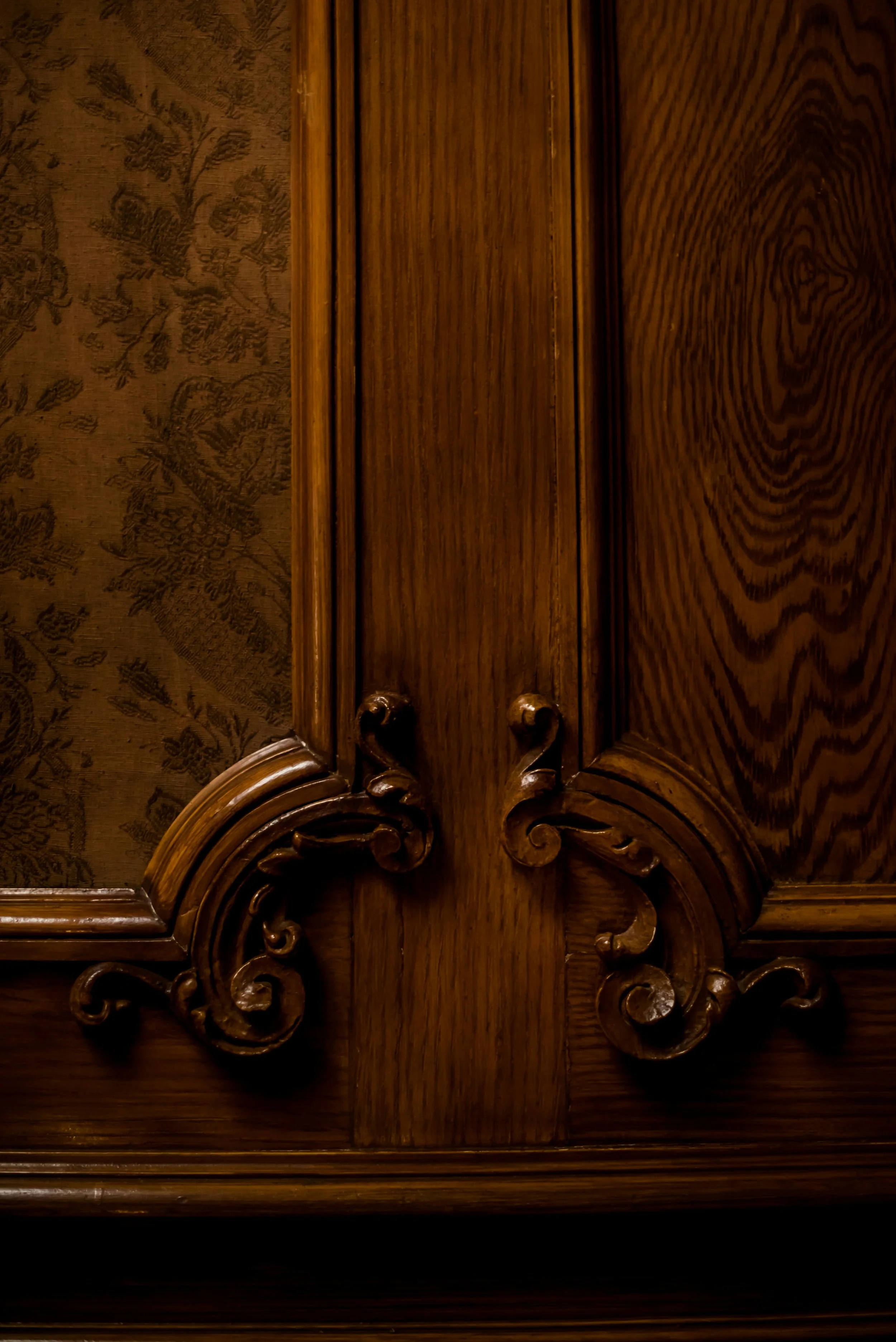 Close-up of a carved wooden piece with ornate scrollwork, set against a background of patterned fabric.
