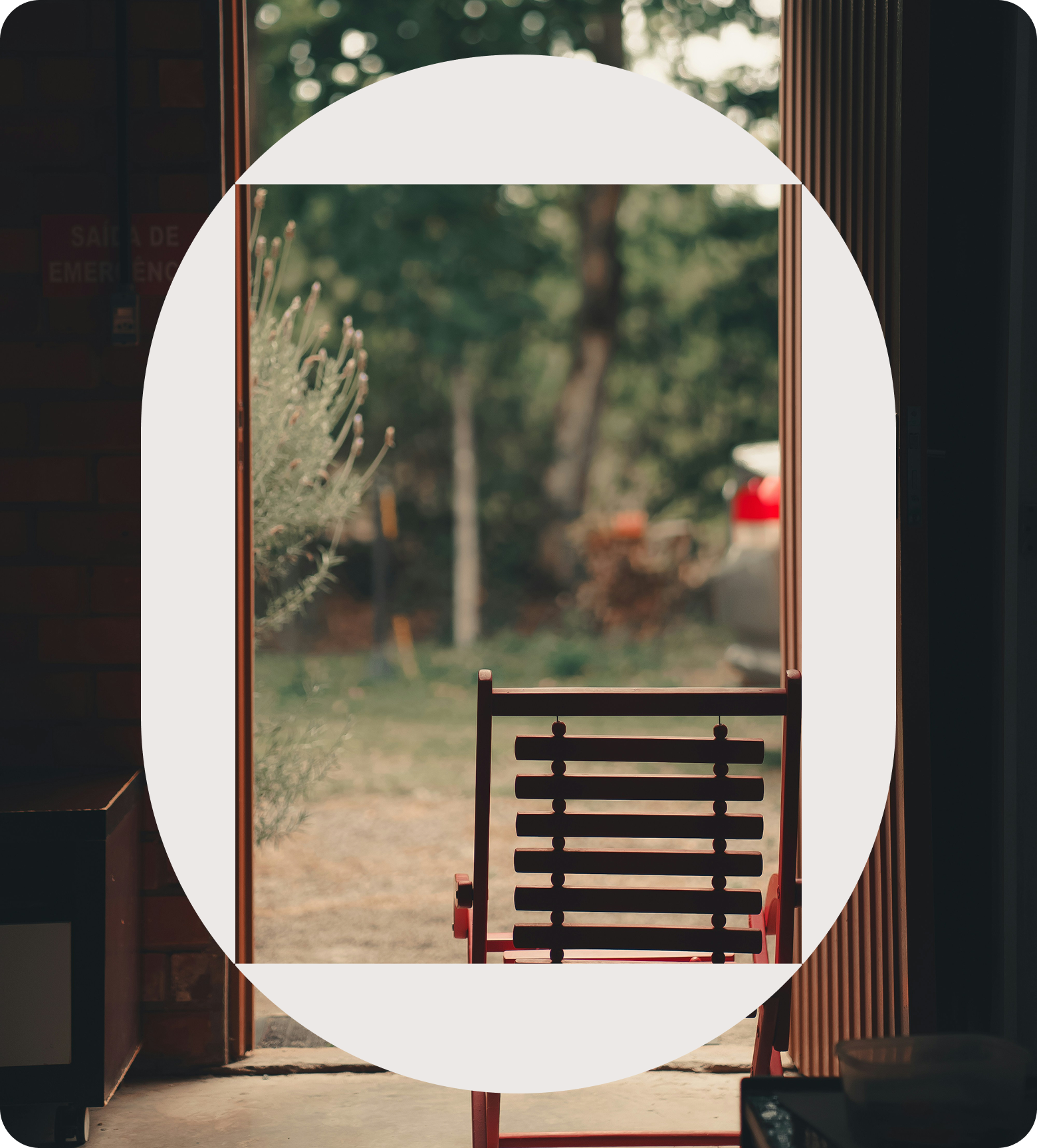View through an open door to a yard with trees, a red fire hydrant, and a car in the background. Inside, a red wooden chair is in the foreground.