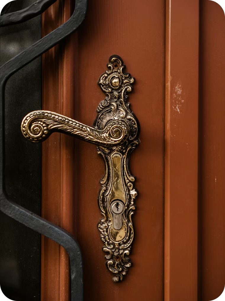 Close-up of an ornate antique brass door handle and keyhole on a brown door.