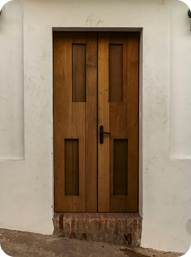A wooden door with four vertical glass panels, black handle, set in a white wall with a brick threshold.