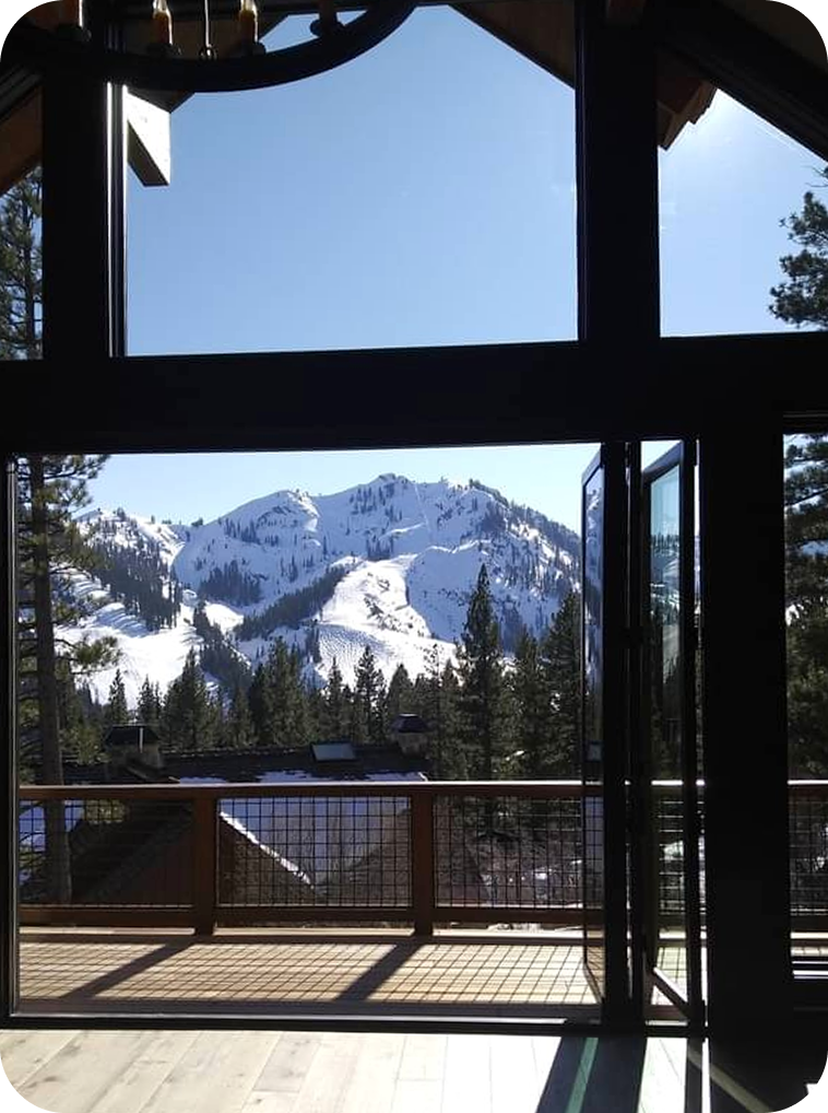 View of snow-covered mountains through a large window with a balcony railing in the foreground.