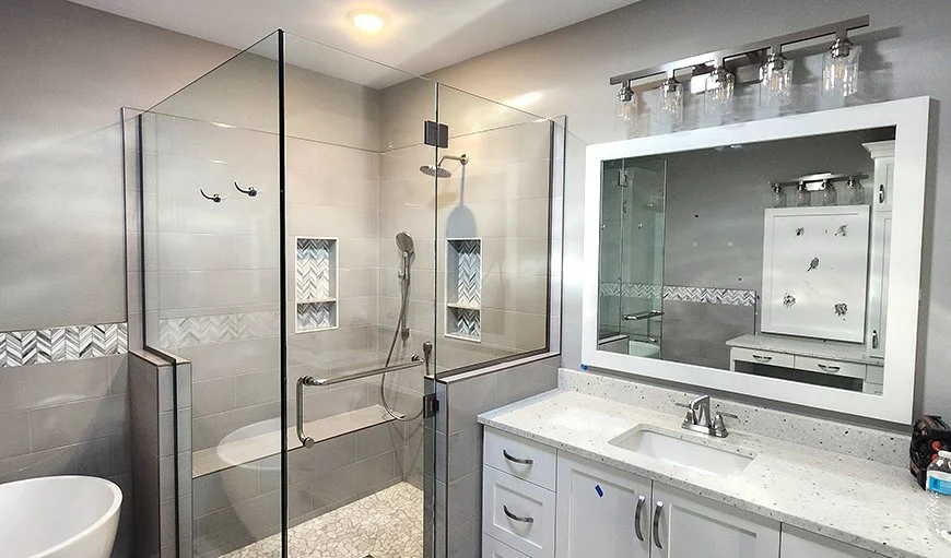 Bathroom with a glass shower enclosure, a white vanity with a speckled countertop, a large mirror, and a wall-mounted light fixture.