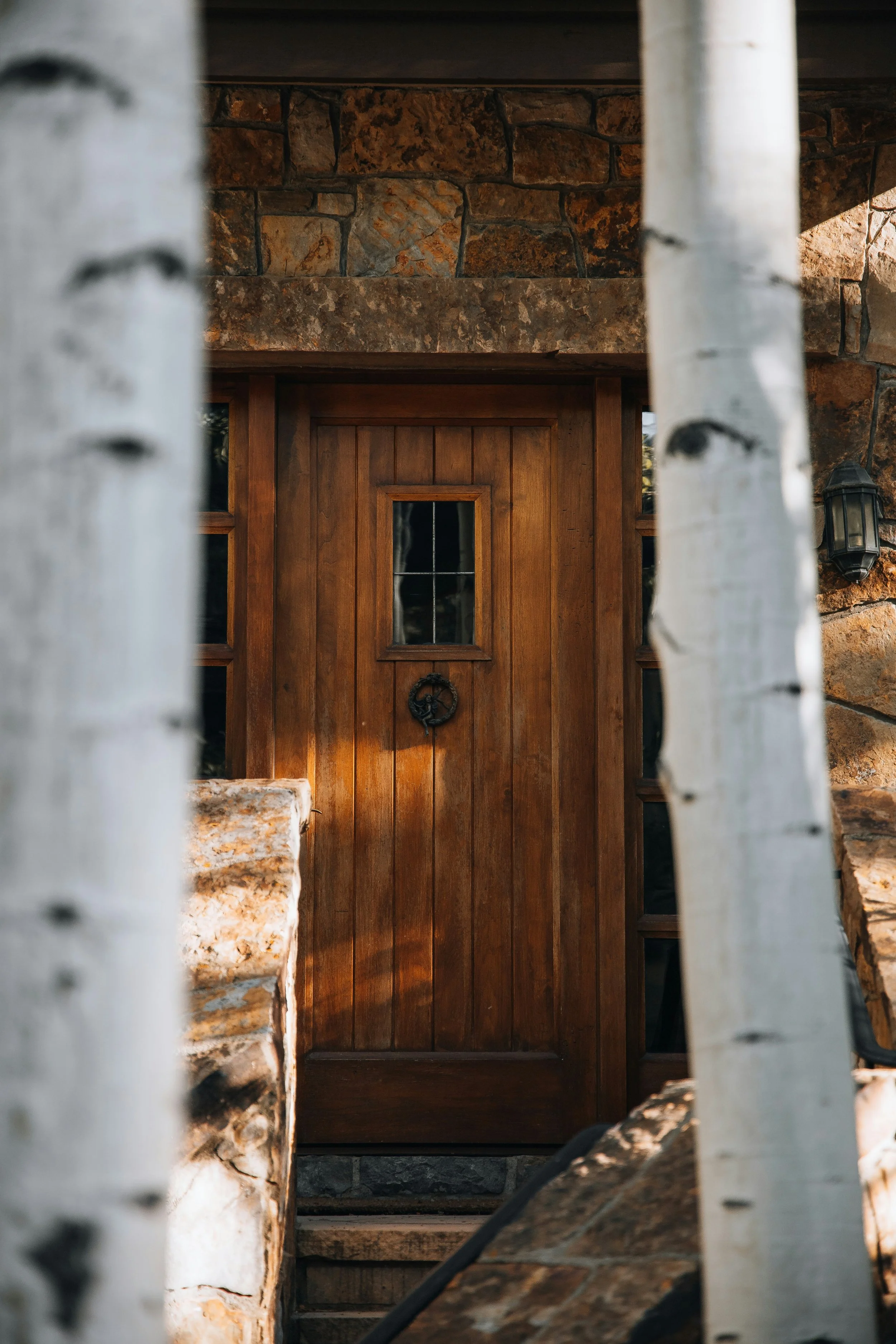 View of a wooden door framed by stone and white painted wood, with steps and a lantern on the right side.