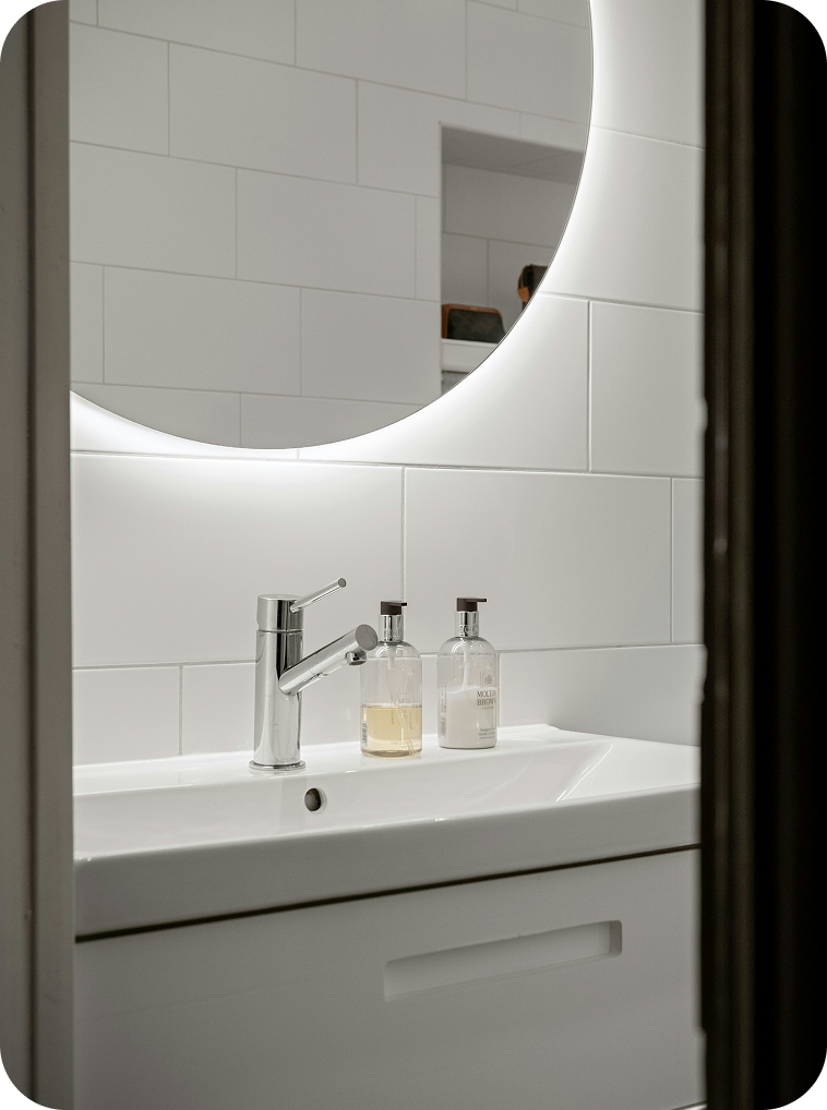 Bathroom mirror above a white sink with two soap dispensers, one filled with liquid soap and the other labeled as moisturizer, with a reflection of a person in the mirror.