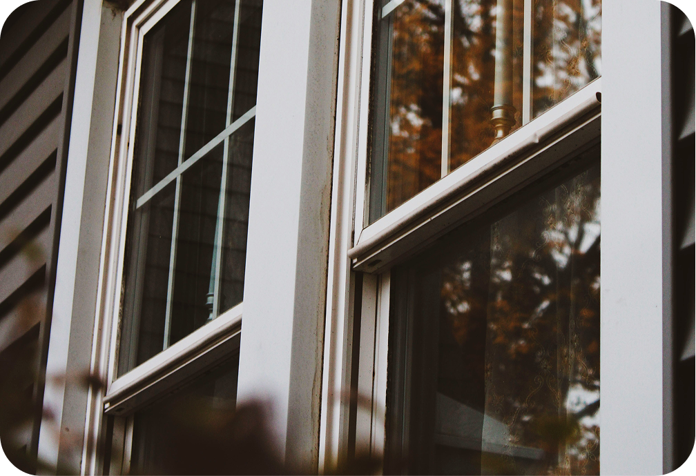 Close-up of a double-pane window on a house with reflection of trees and sky in the glass.