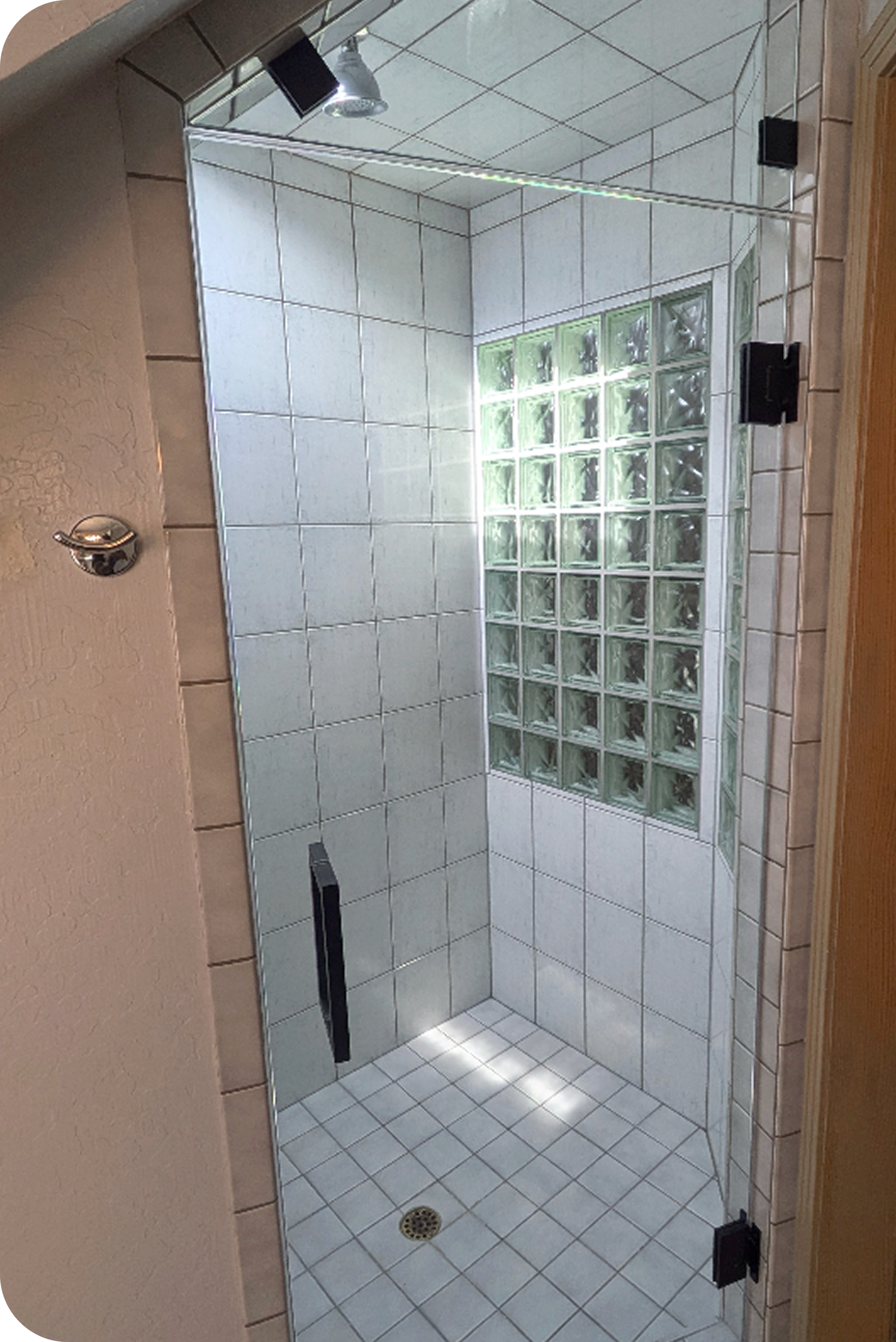 Empty shower stall with white tiled walls, glass block window for natural light, and a drain on the tiled floor.