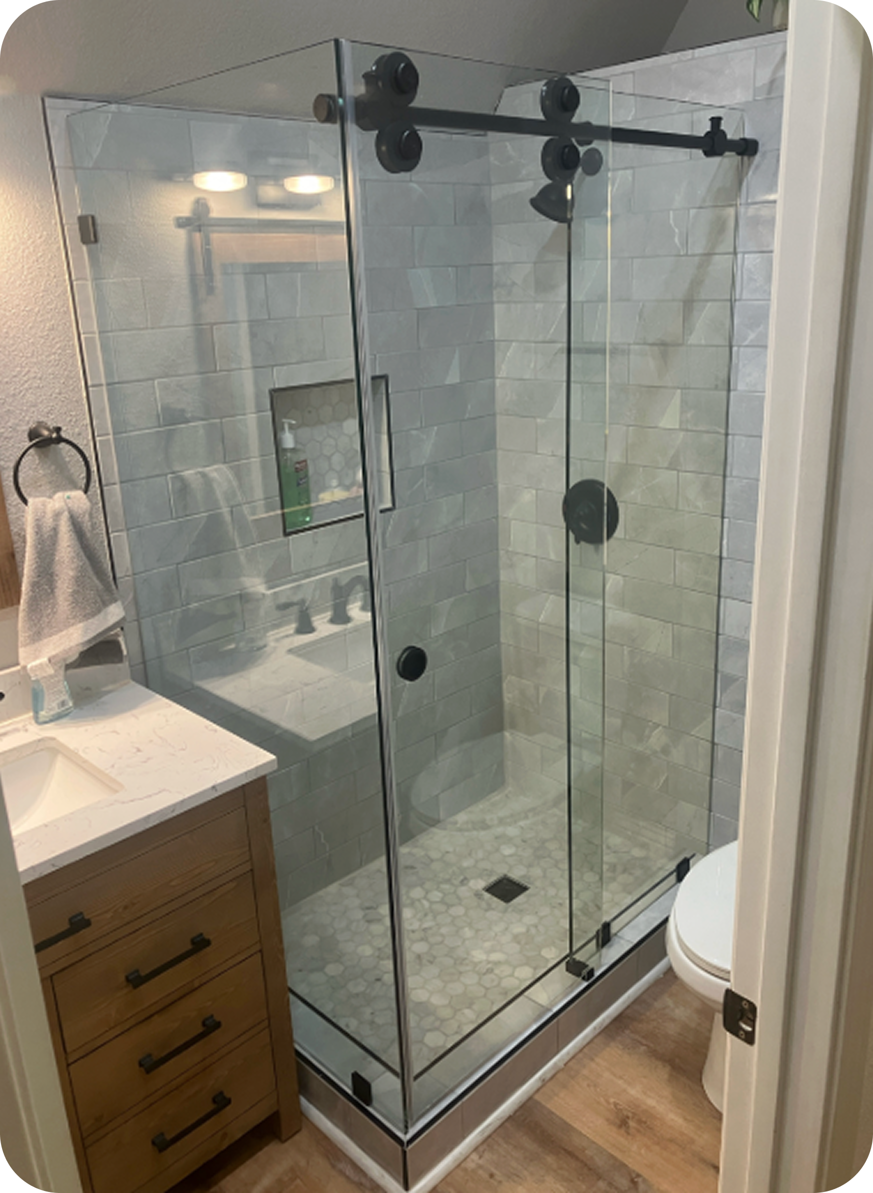 Bathroom with glass shower enclosure, marble tiles, wooden vanity with drawers, and a white bathroom fixture.