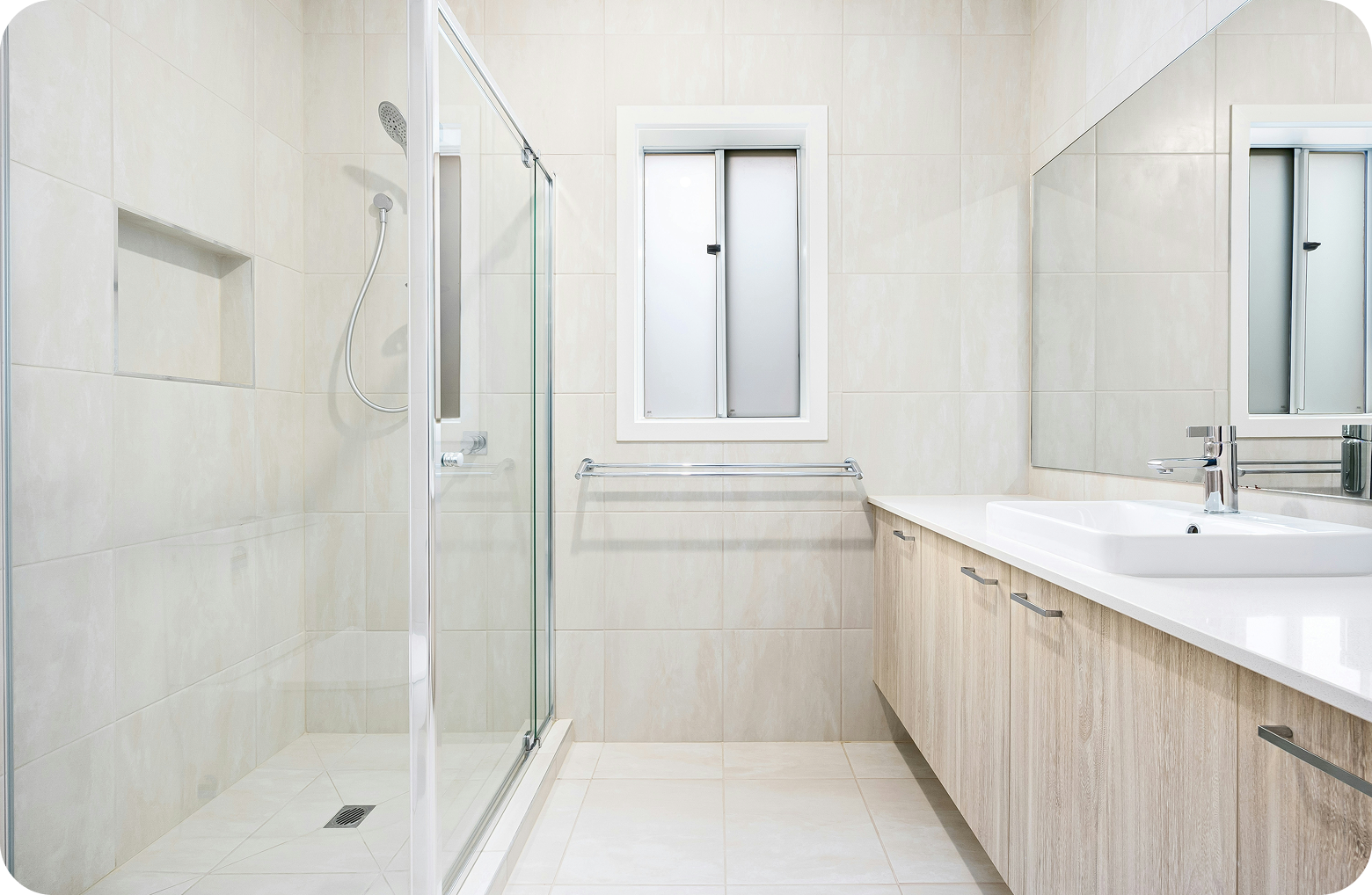 Clean, modern bathroom with a glass-enclosed shower on the left, a white vanity with a sink and a large mirror on the right, and a small frosted window in the center.