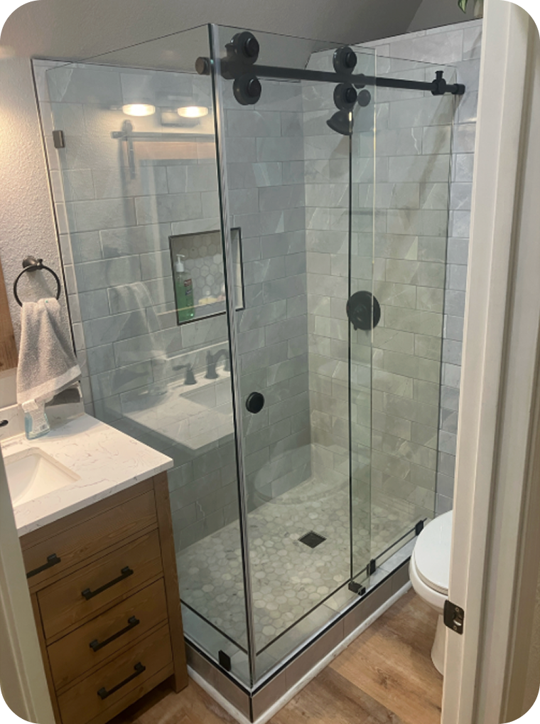 A glass shower enclosure with sliding doors, a niche for toiletries inside, and a pebble tile floor, located next to a wooden vanity with a white countertop in a bathroom.