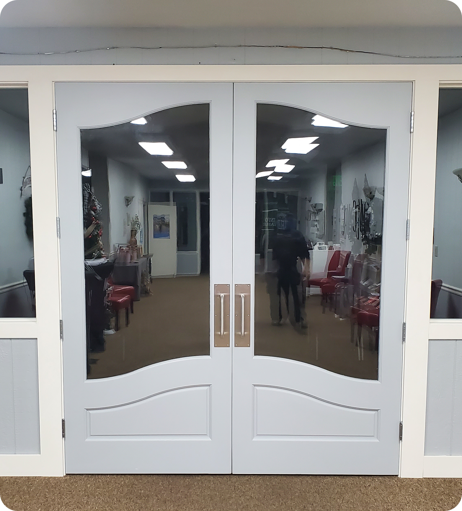 Double glass doors with white frames revealing a room with chairs, tables, and a person walking inside.