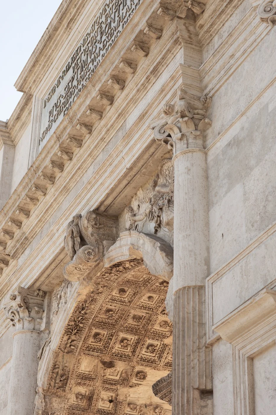 Close-up of ancient stone archway with ornate carvings and Greek-style columns, part of a historic classical building.